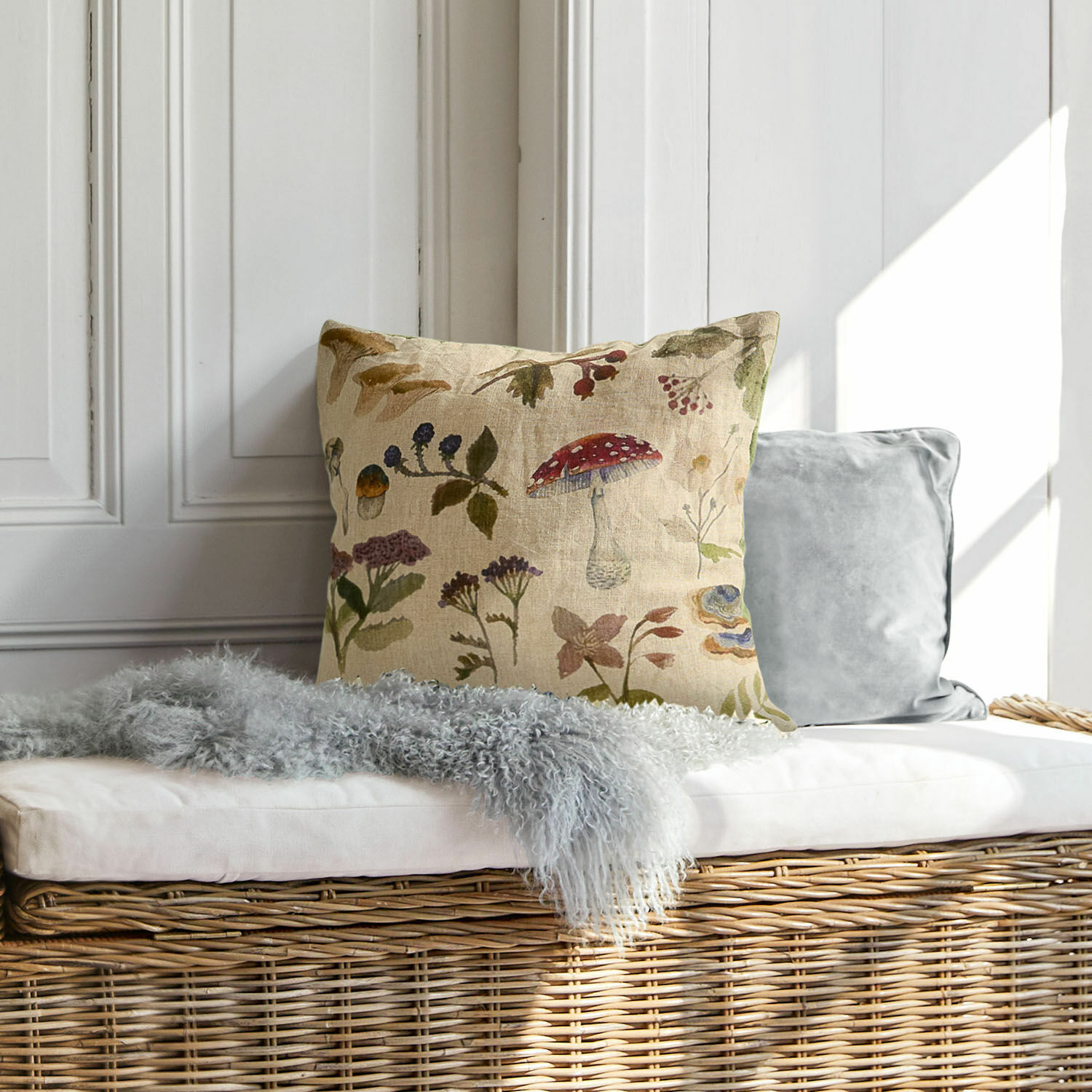 Housse de coussin Selarune Coussin décoratif en lin avec motif végétal naturel posé sur un banc en osier clair