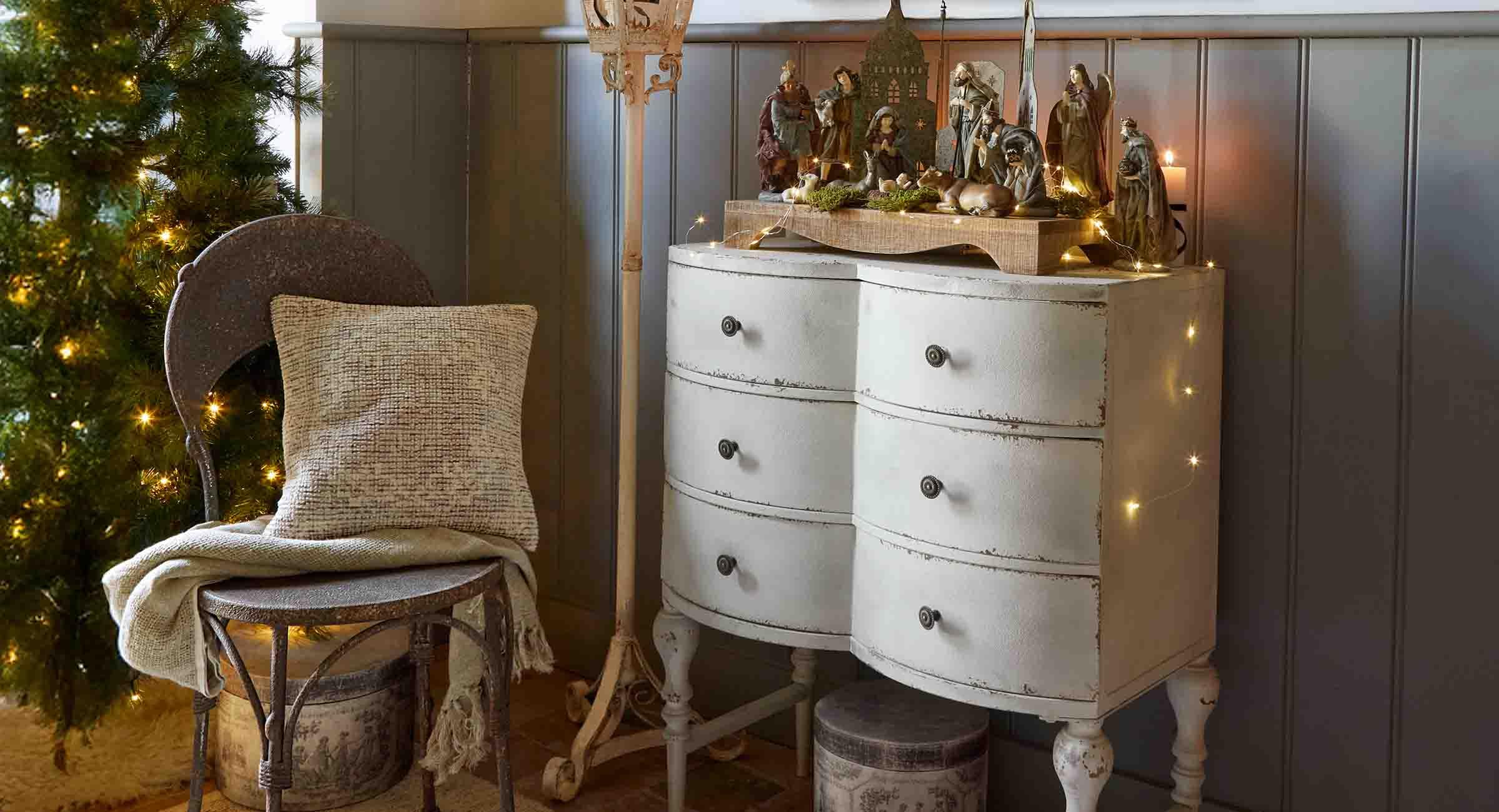 Commode blanche vieillie avec crèche en bois et décorations de Noël dans un intérieur chaleureux et cosy