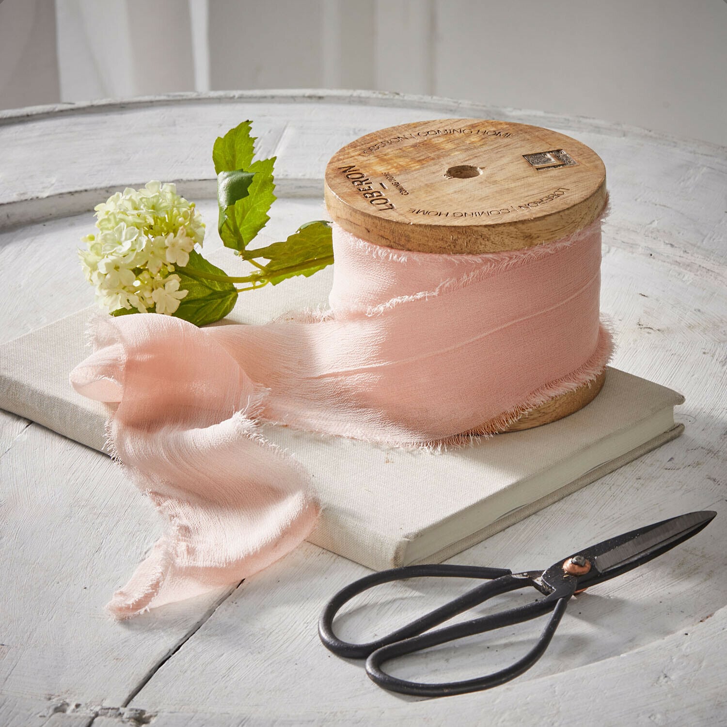 Lint Lunebrook Roze stoffen lint op houten spoel met schaar en bloem op witte tafel