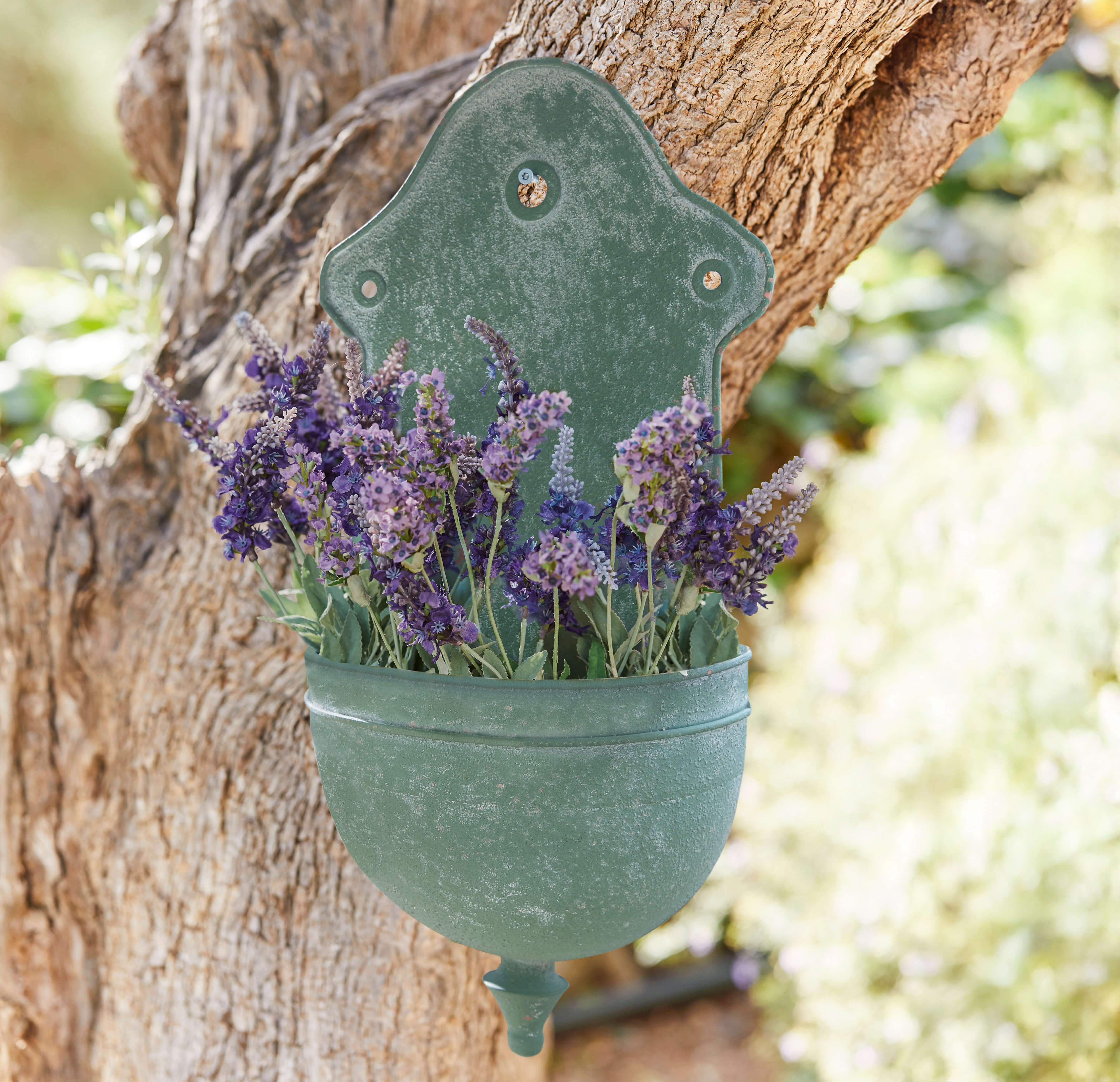 Groene metalen wandbloempot met paarse lavendelbloemen tegen boom, tuindecoratie