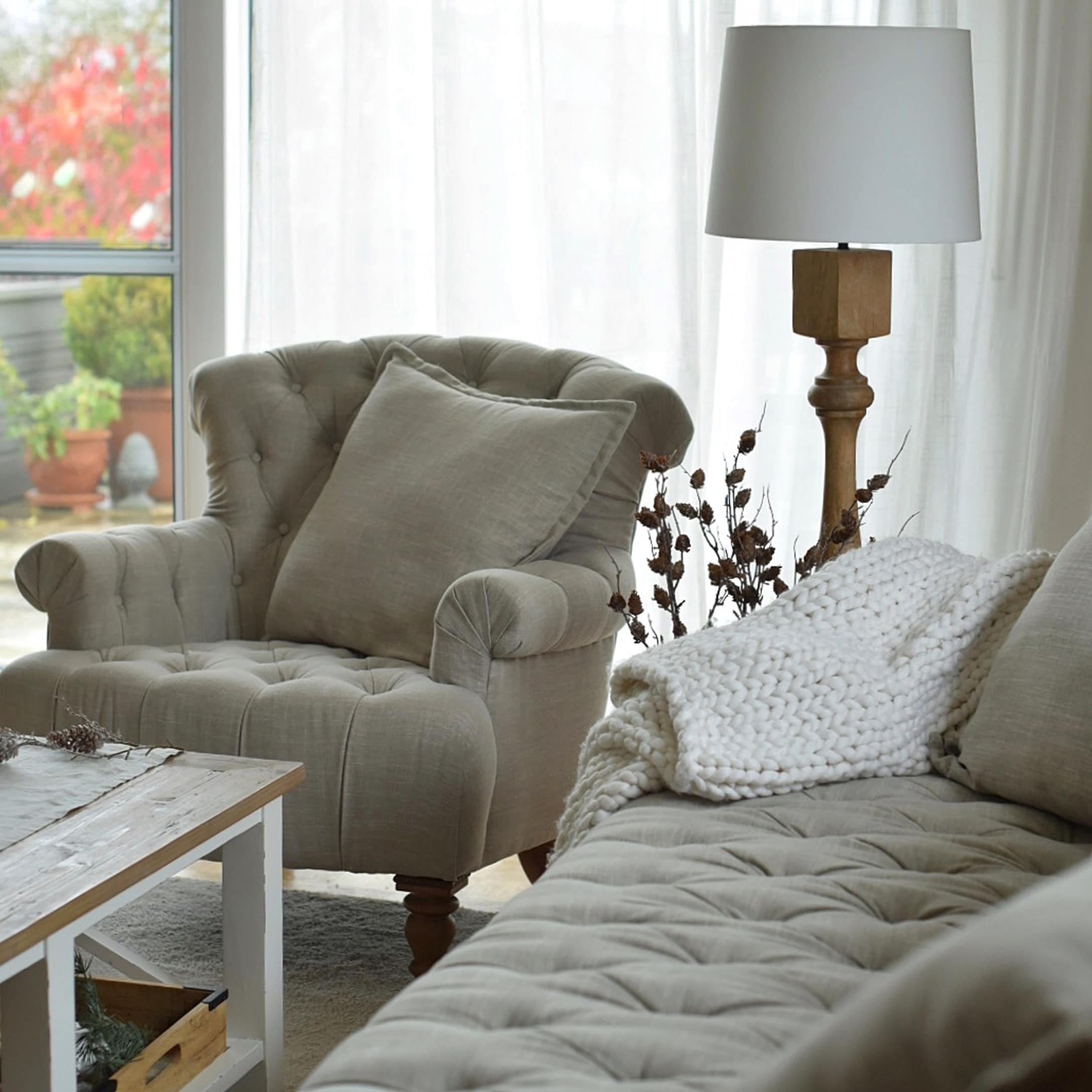 Fauteuil et canapé beige rembourrés avec coussins et plaid tricoté blanc dans un salon chaleureux