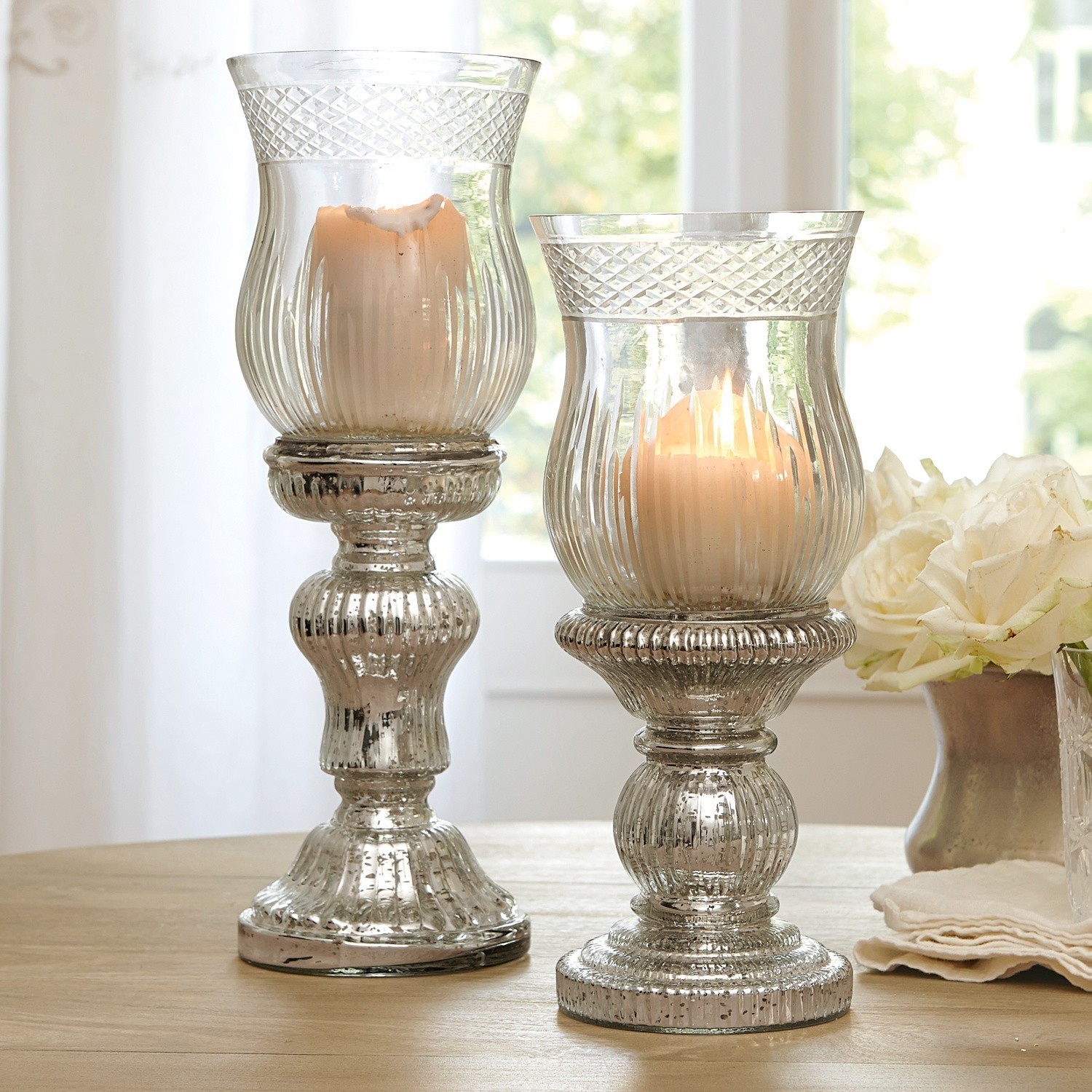 Lot de 2 bougeoirs Luisant Deux bougeoirs décoratifs en verre effet argent vieilli posés sur une table en bois dans un intérieur lumineux