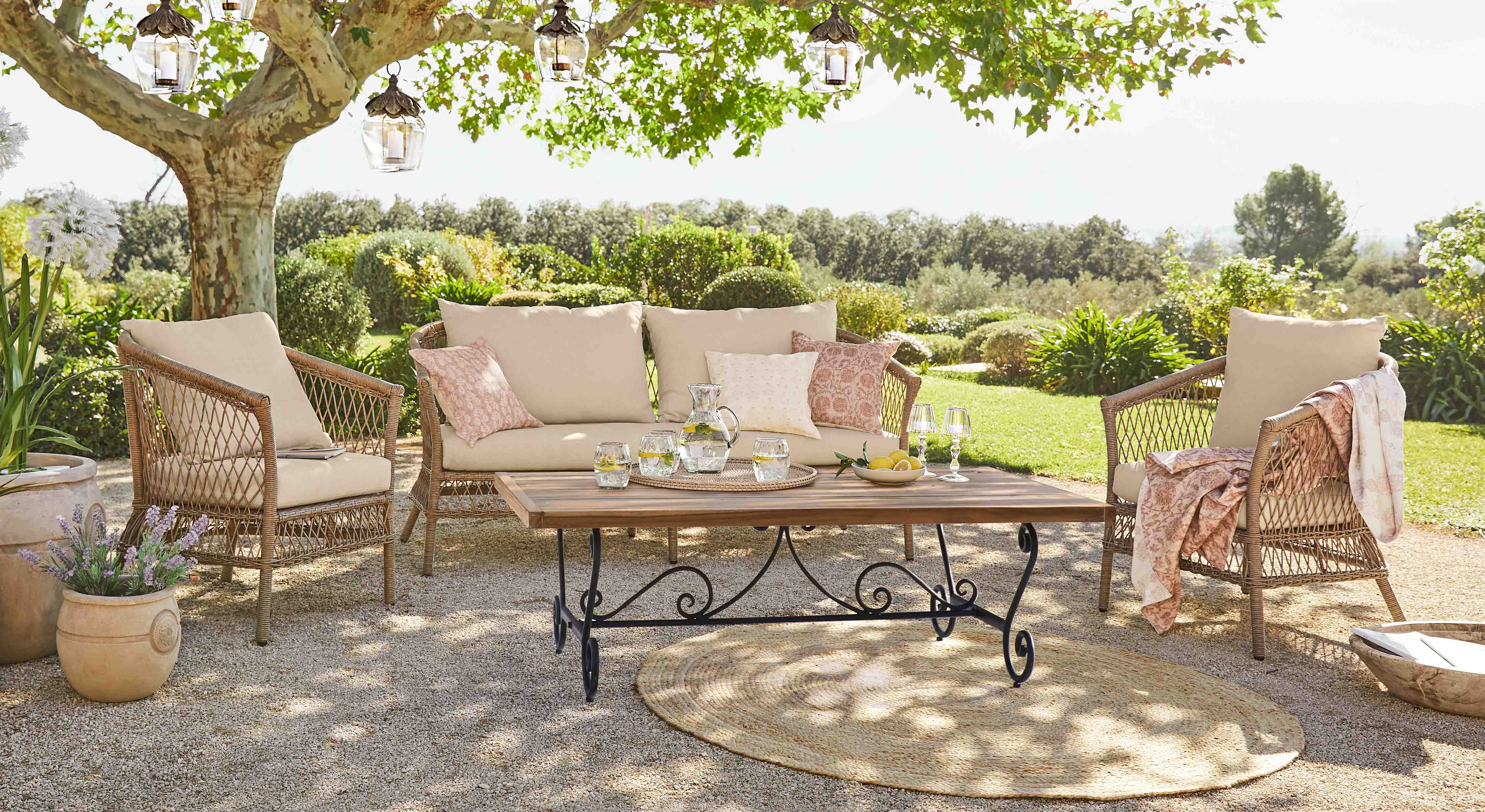 Tuinmeubelset van rattan met beige kussens en houten tafel op zonnig terras in tuin