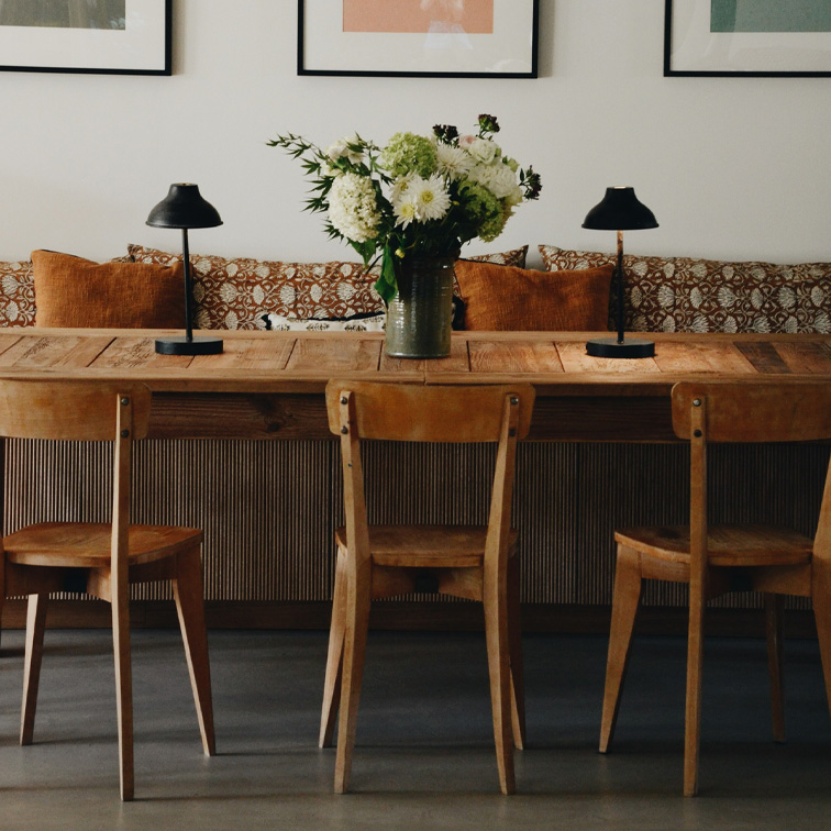 Table en bois avec trois chaises, lampes noires et vase de fleurs blanches dans un salon chaleureux