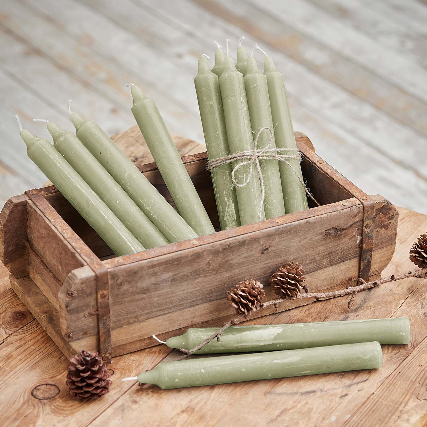 Set groene waskaarsen in houten doos op rustieke houten tafel met dennenappels