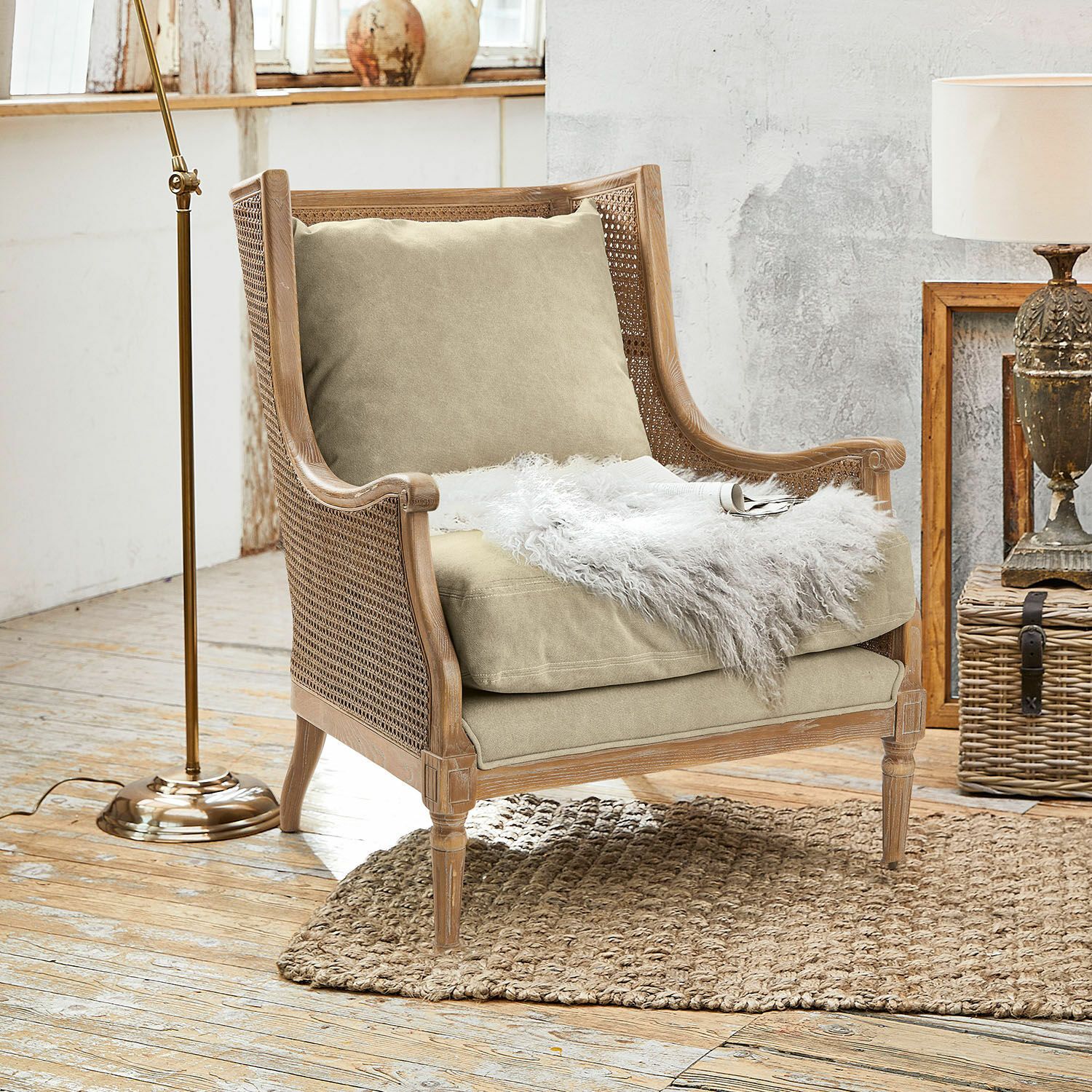 Fauteuil Greenbrier Fauteuil en bois et rotin avec coussin beige et plaid en fausse fourrure blanche sur tapis naturel