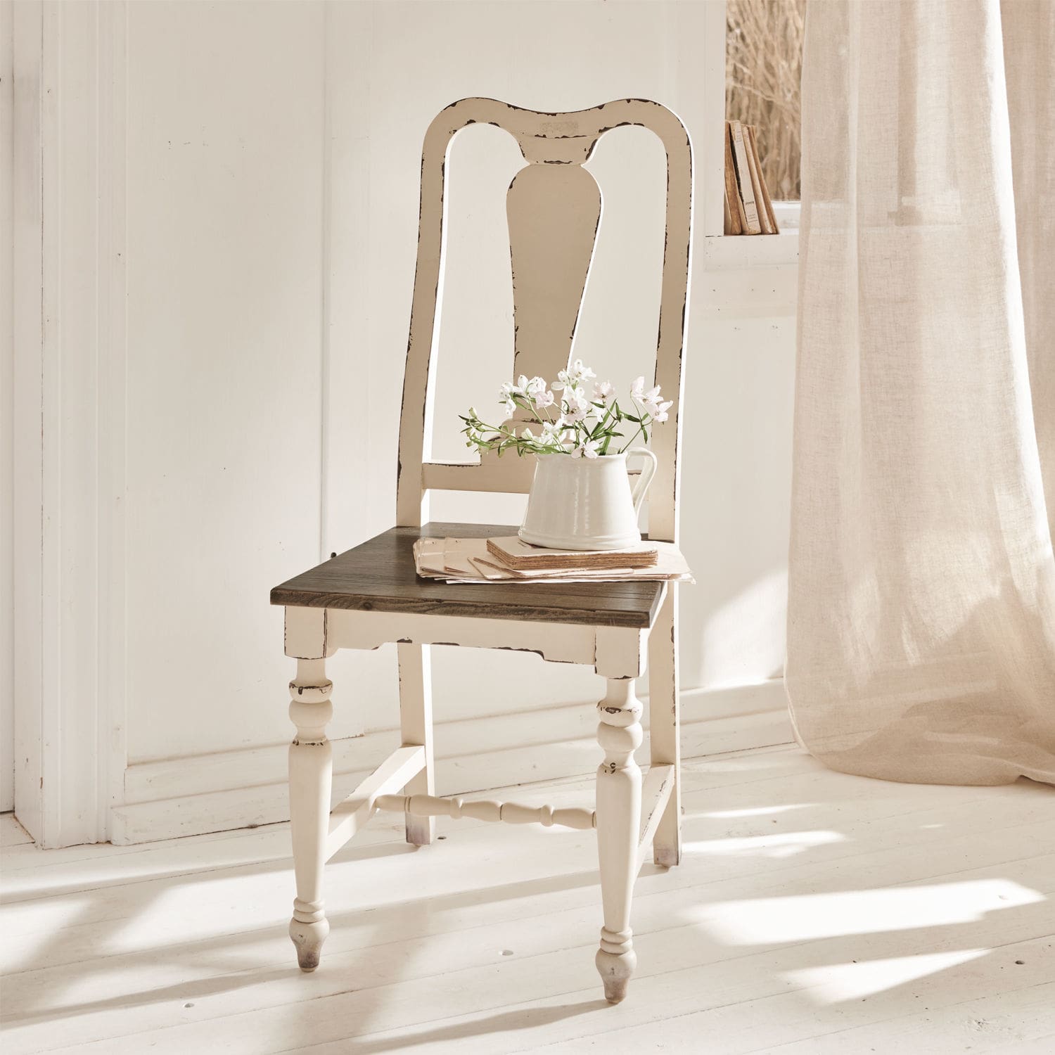 Chaise Harry Chaise vintage en bois blanc avec assise foncée et pichet à fleurs dans une pièce lumineuse