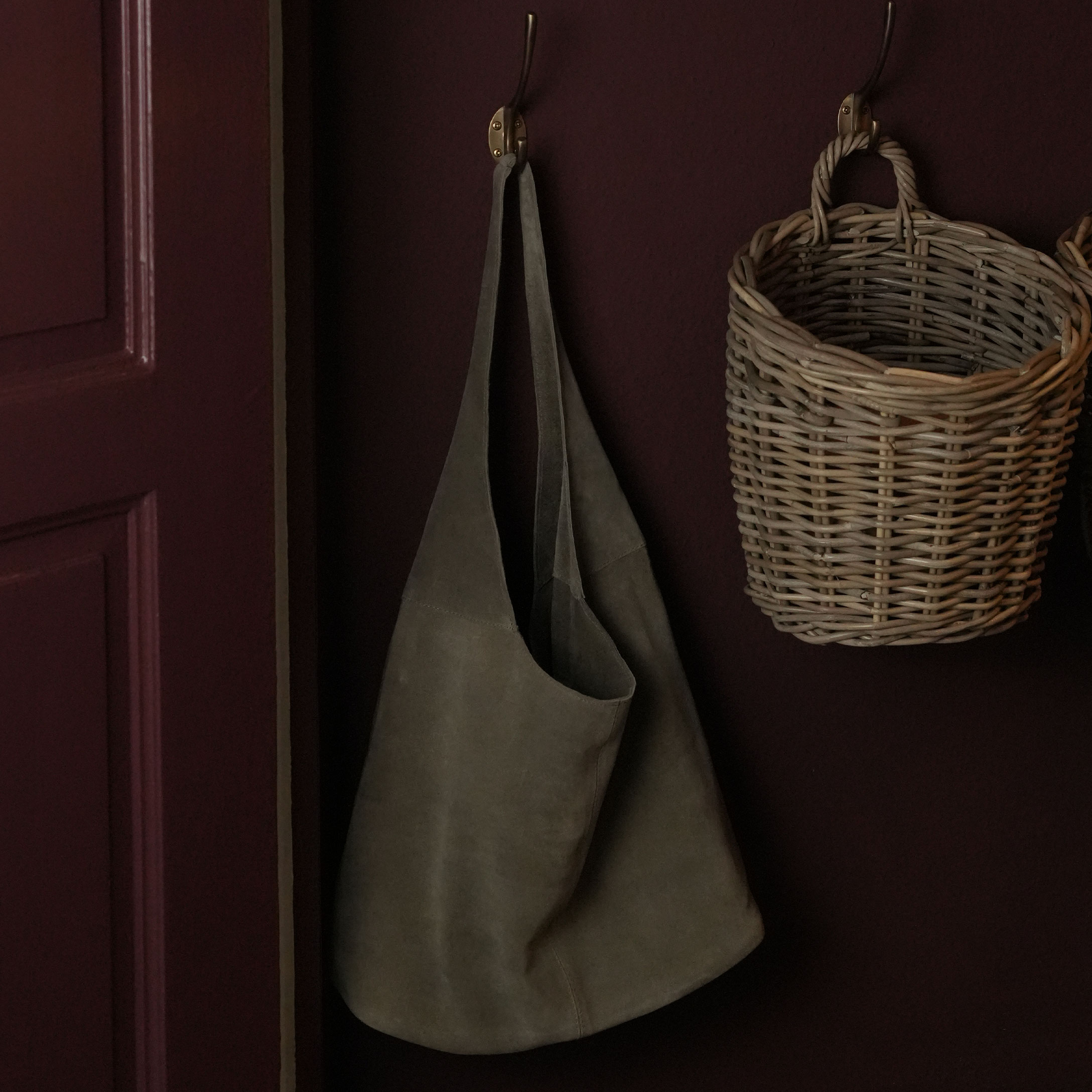Tablier en daim gris suspendu à un crochet en cuivre à côté d'un panier en osier sur un mur sombre