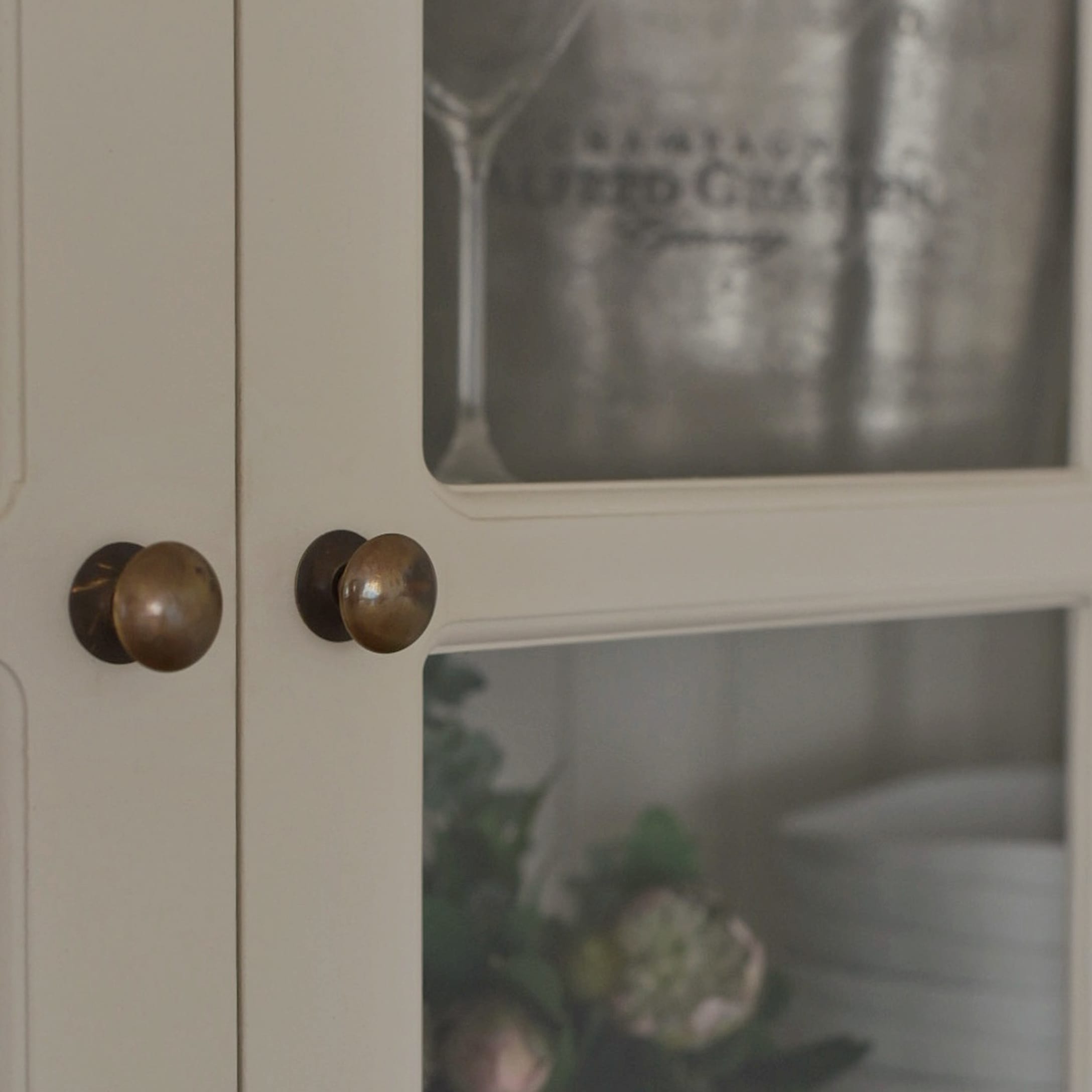 Détail d'une armoire blanche en bois avec poignées en laiton et portes vitrées pour vaisselle