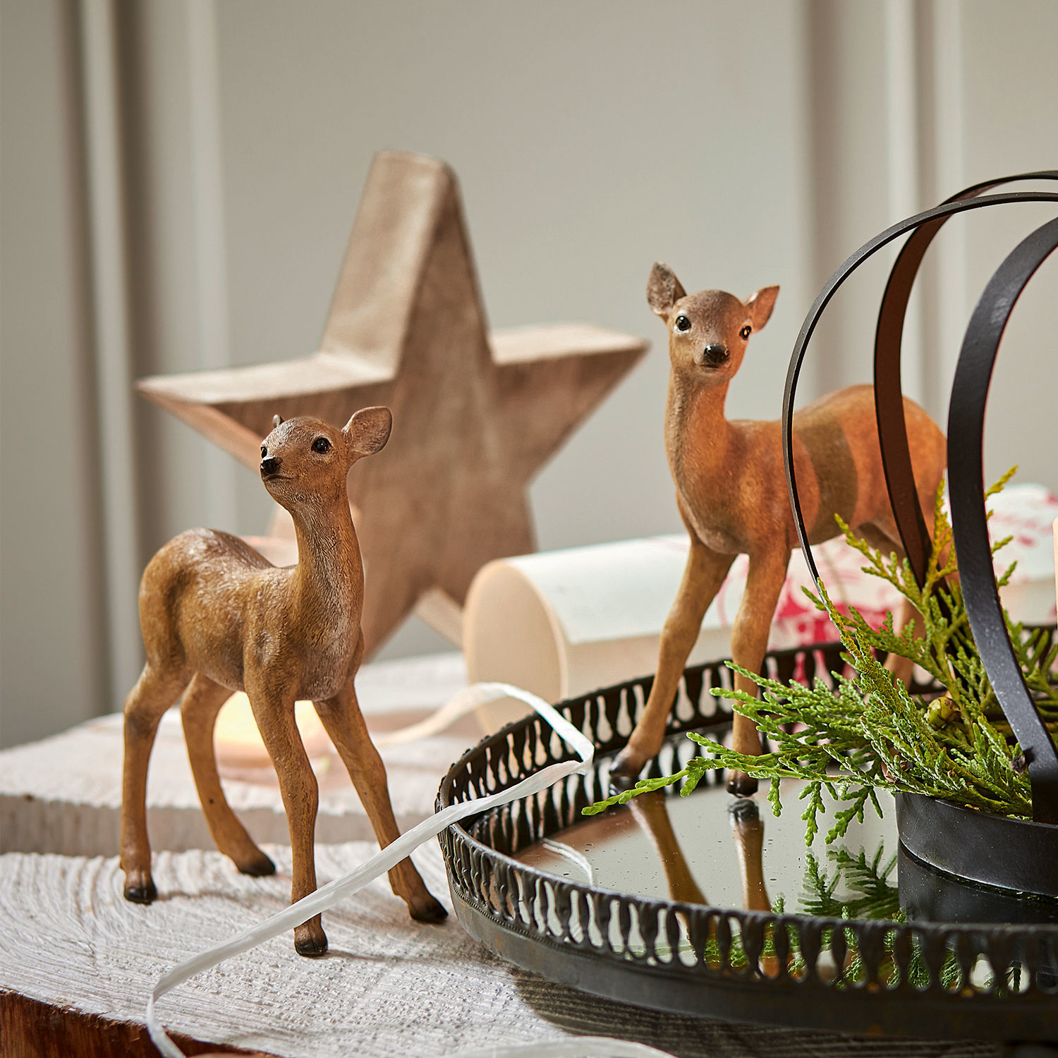 Deux figurines de faons marron sur une table en bois avec un plateau en métal et des branches vertes décoratives
