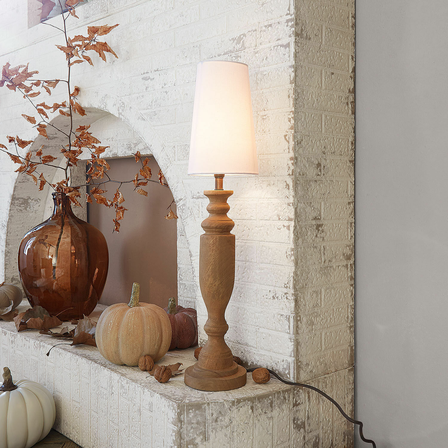 Lampe à poser Ambrevaux Lampe de table en bois avec abat-jour blanc devant un mur en briques blanches et décorations d'automne