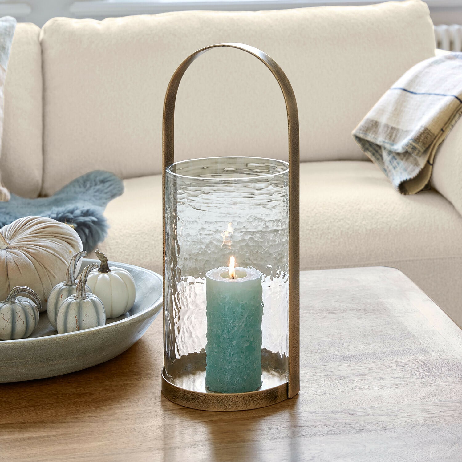 Windlicht Omirah Glazen lantaarn met messing handvat en blauwe kaars op houten tafel in woonkamer