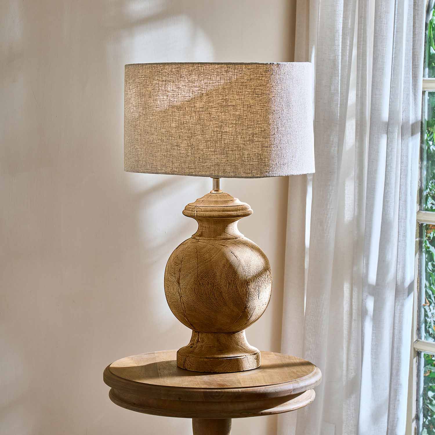 Tafellamp met houten voet en beige kap op ronde houten tafel bij raam