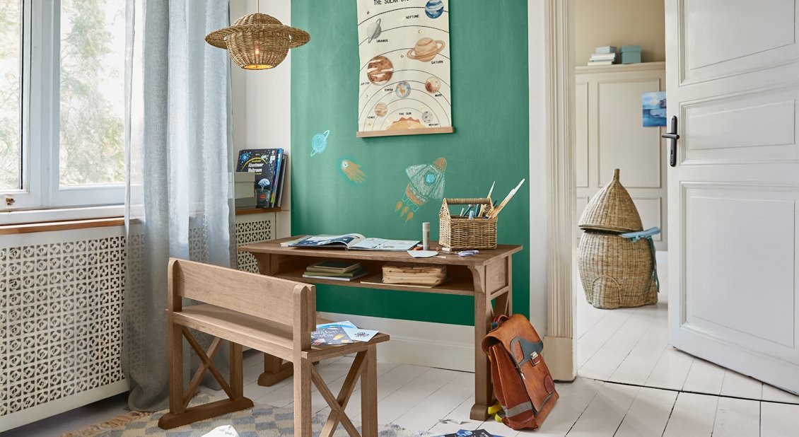 Bureau et banc en bois dans une chambre d'enfant avec mur vert et panier en osier pour fournitures scolaires