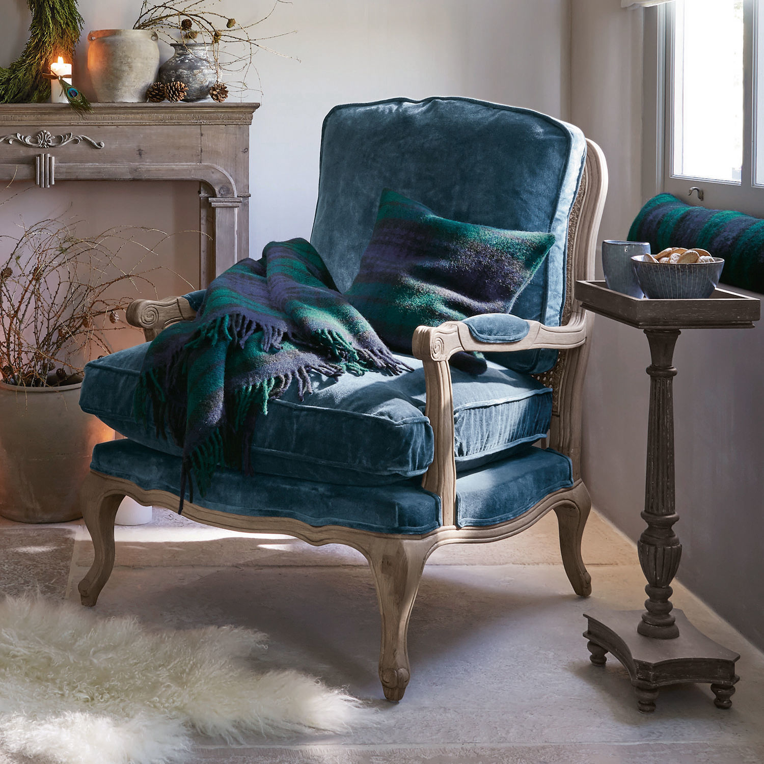 Blauwe fluwelen fauteuil met lichte houten frame, groene en blauwe deken en kussen in gezellige kamer