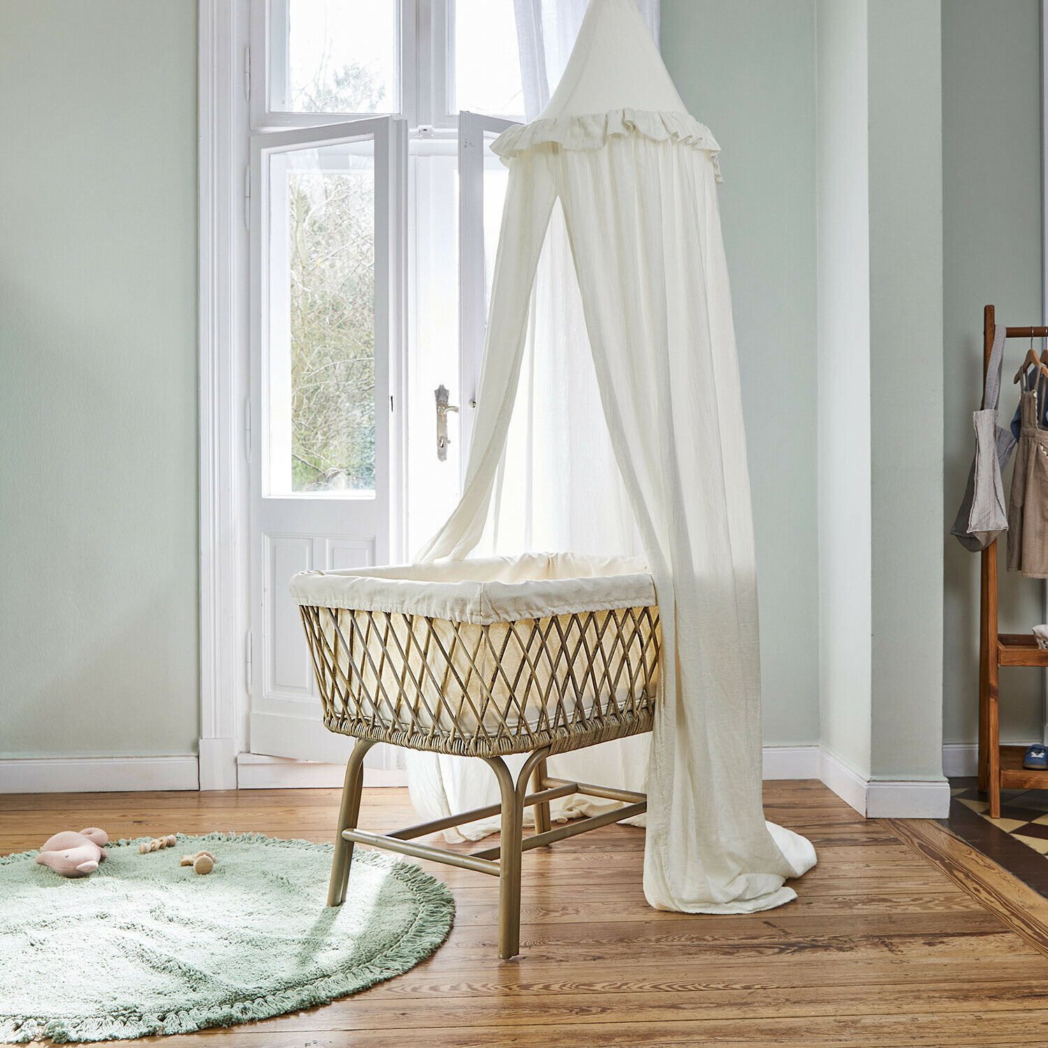 Ciel de lit Nuvinas Berceau en rotin naturel avec voilage blanc léger suspendu dans une chambre d'enfant lumineuse