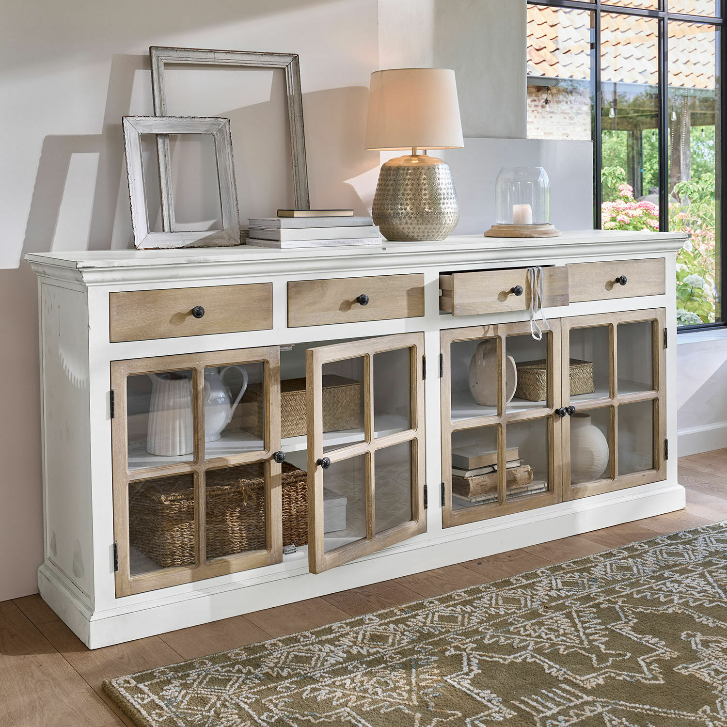 Commode Marshwood Buffet en bois blanc avec tiroirs et portes vitrées, décorations et lampe posées dessus