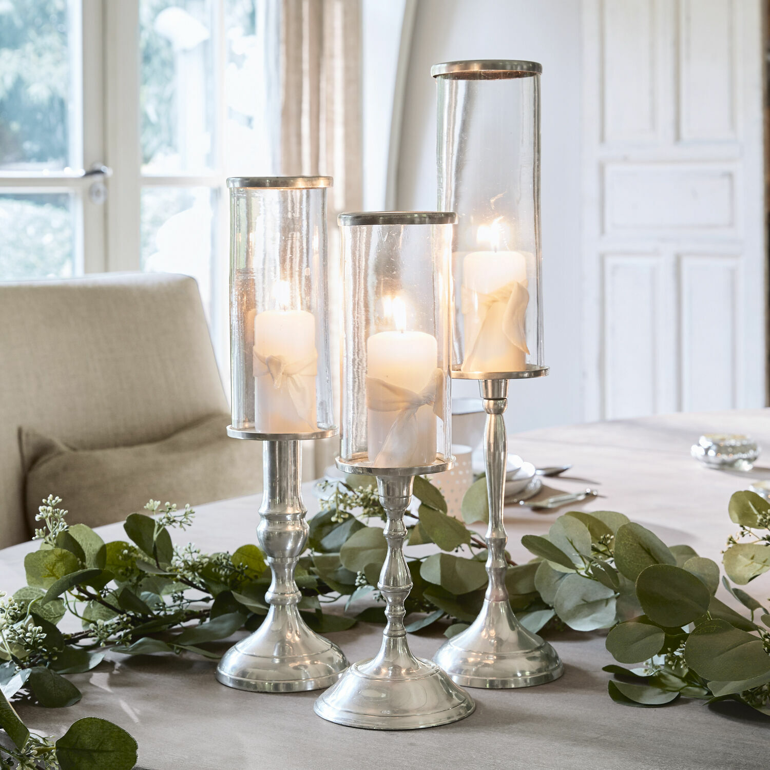 Set van drie zilverkleurige kandelaren van glas en metaal met witte kaarsen als tafeldecoratie