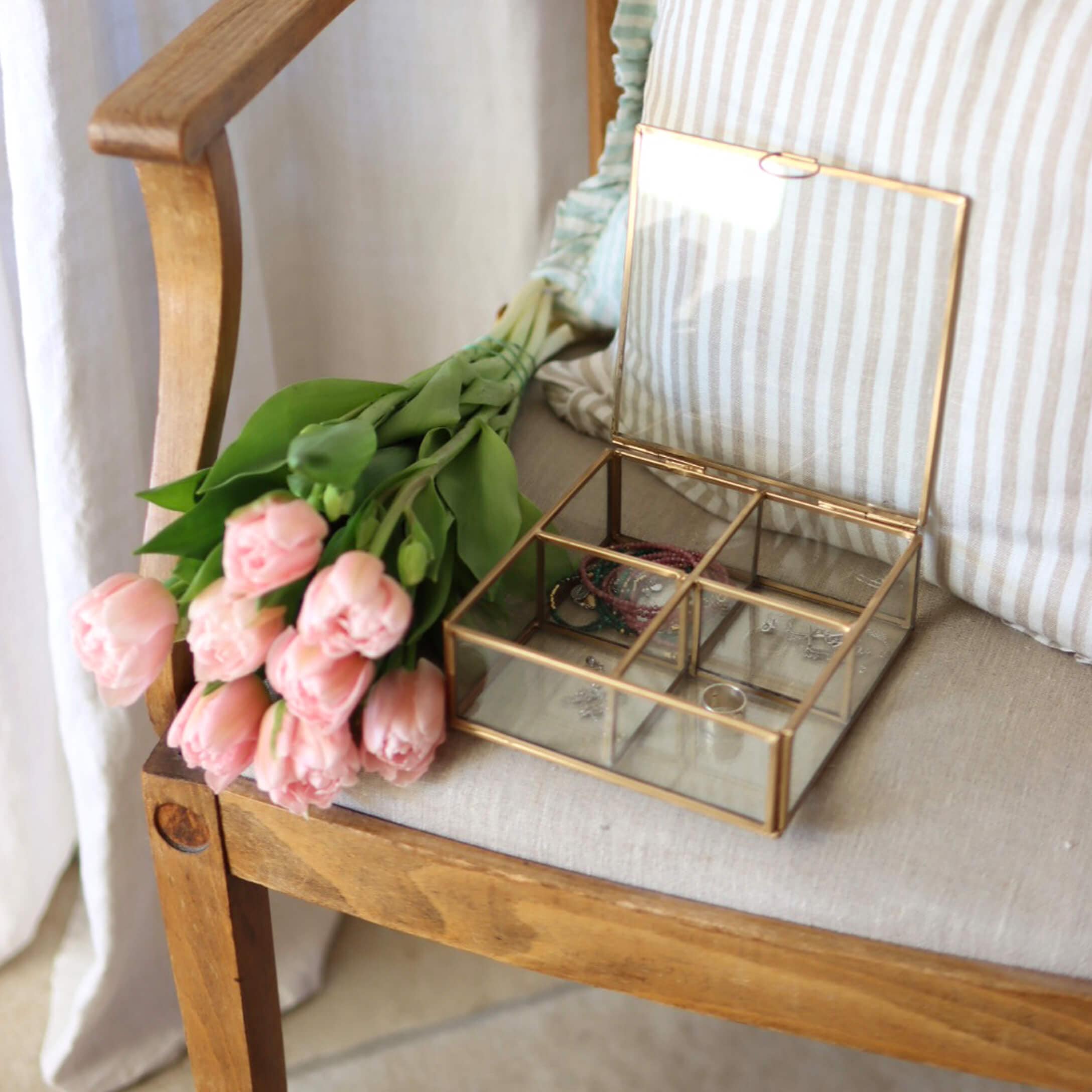Boîte à bijoux en verre avec cadre en laiton sur chaise en bois à côté de tulipes roses