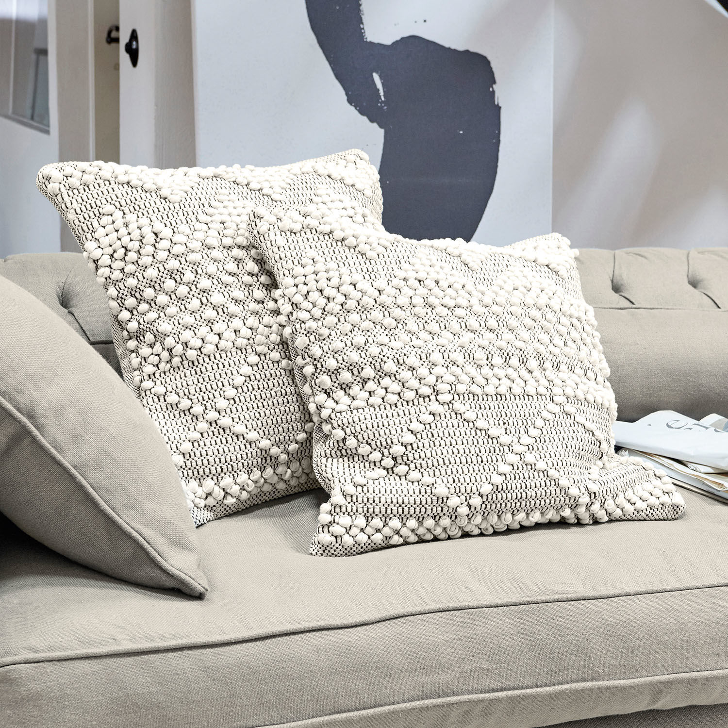 Lot de 2 housses de coussins Hadir Deux coussins décoratifs crème en coton avec texture et motif géométrique sur un canapé gris
