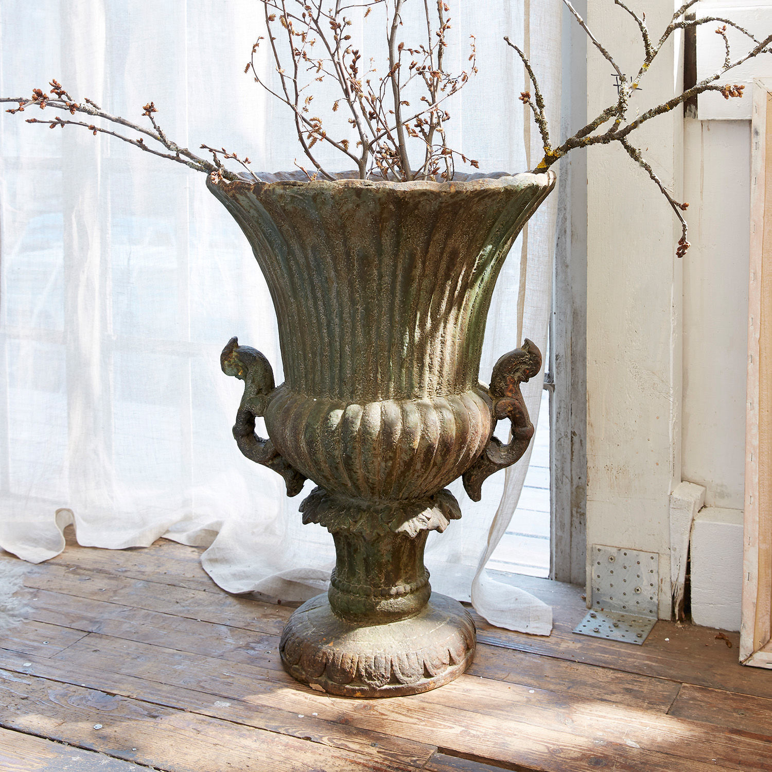 Amfoor Estefanie Grote decoratieve metalen vaas met groene patina op houten vloer met takken
