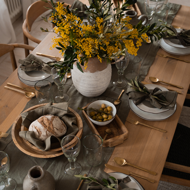 Rustieke houten tafel met wit servies, houten kommen en gele bloemen in een aardewerken vaas