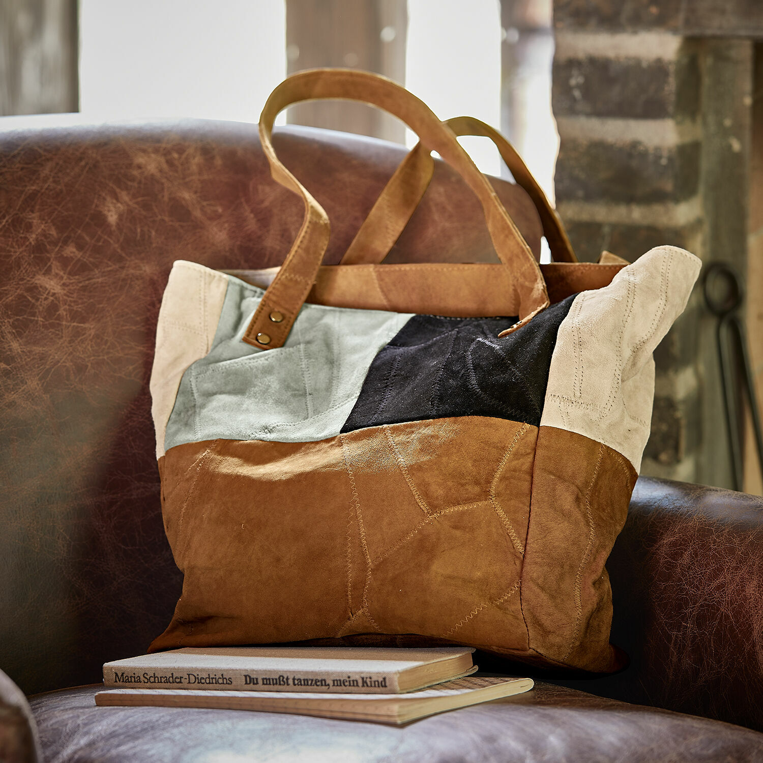Sac Quinvelle Sac patchwork en daim marron, noir et beige posé sur un fauteuil en cuir marron