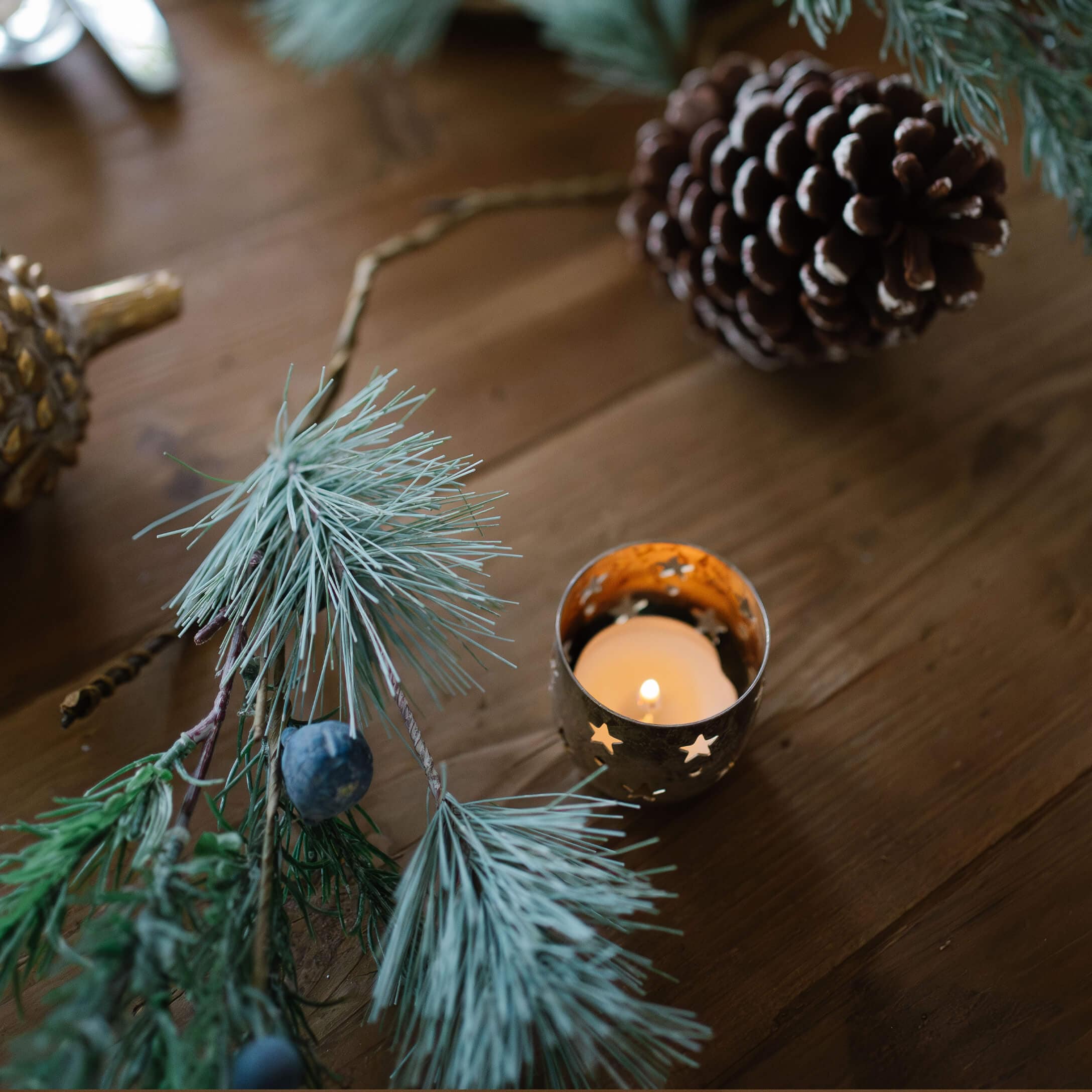 Photophore en métal avec étoiles découpées et bougie allumée sur table en bois avec décoration de pommes de pin et branches