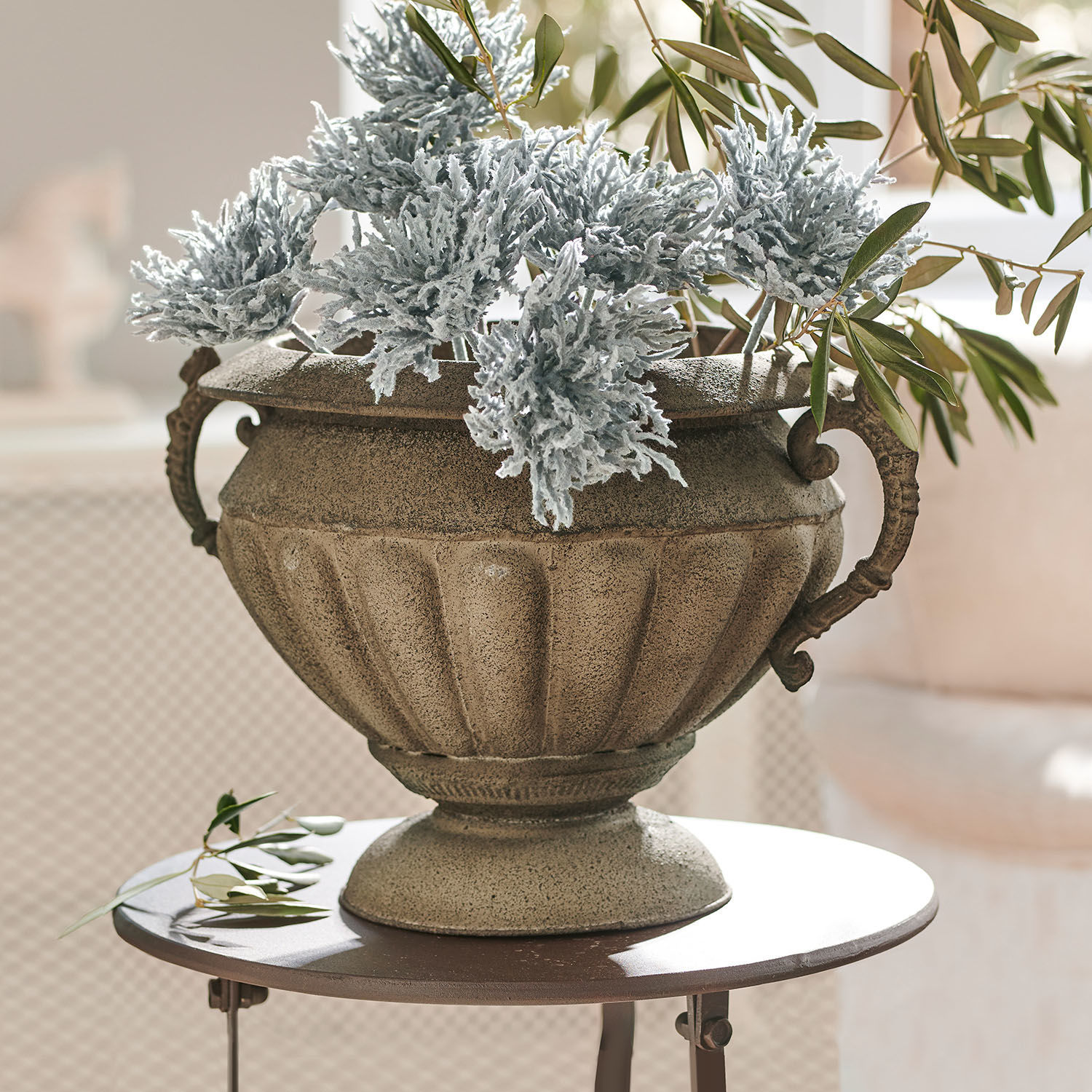 Amfoor Acheville Decoratieve stenen pot in beige met groene en grijze bladeren op een ronde tafel