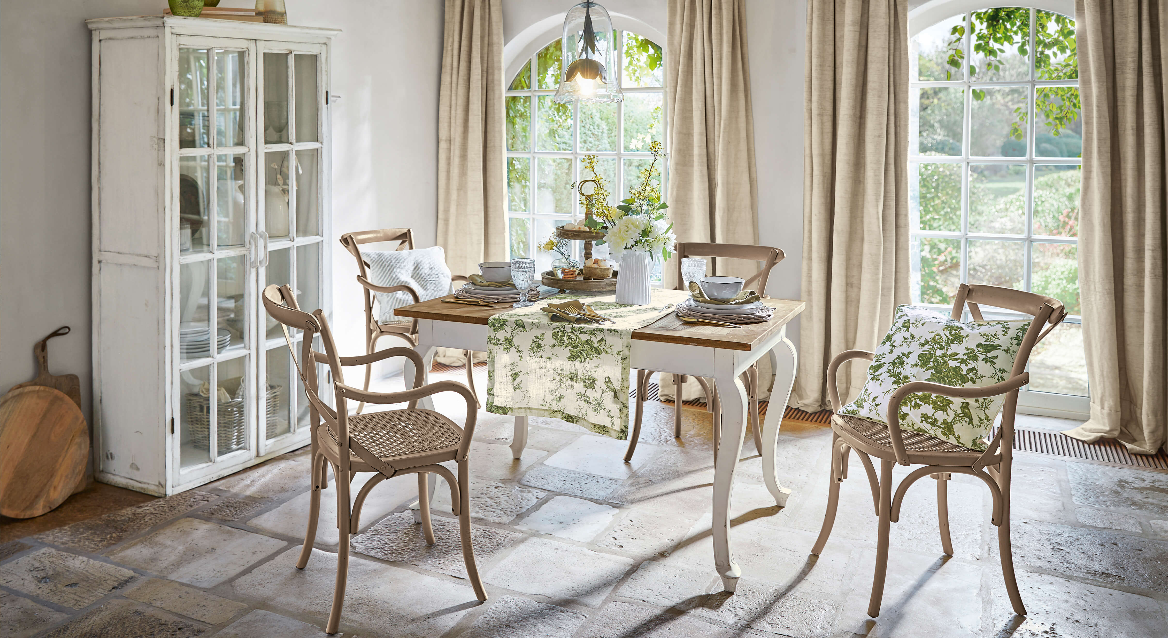 Eetkamer met houten tafel en beige stoelen met groene kussens, natuurlijk licht door ramen