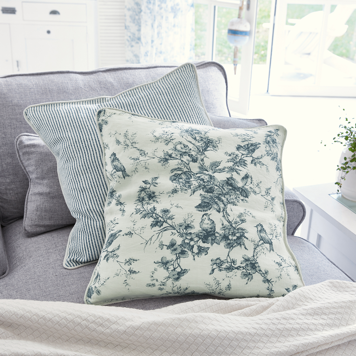 Coussin décoratif réversible en coton avec motifs floraux et rayures bleues sur canapé gris
