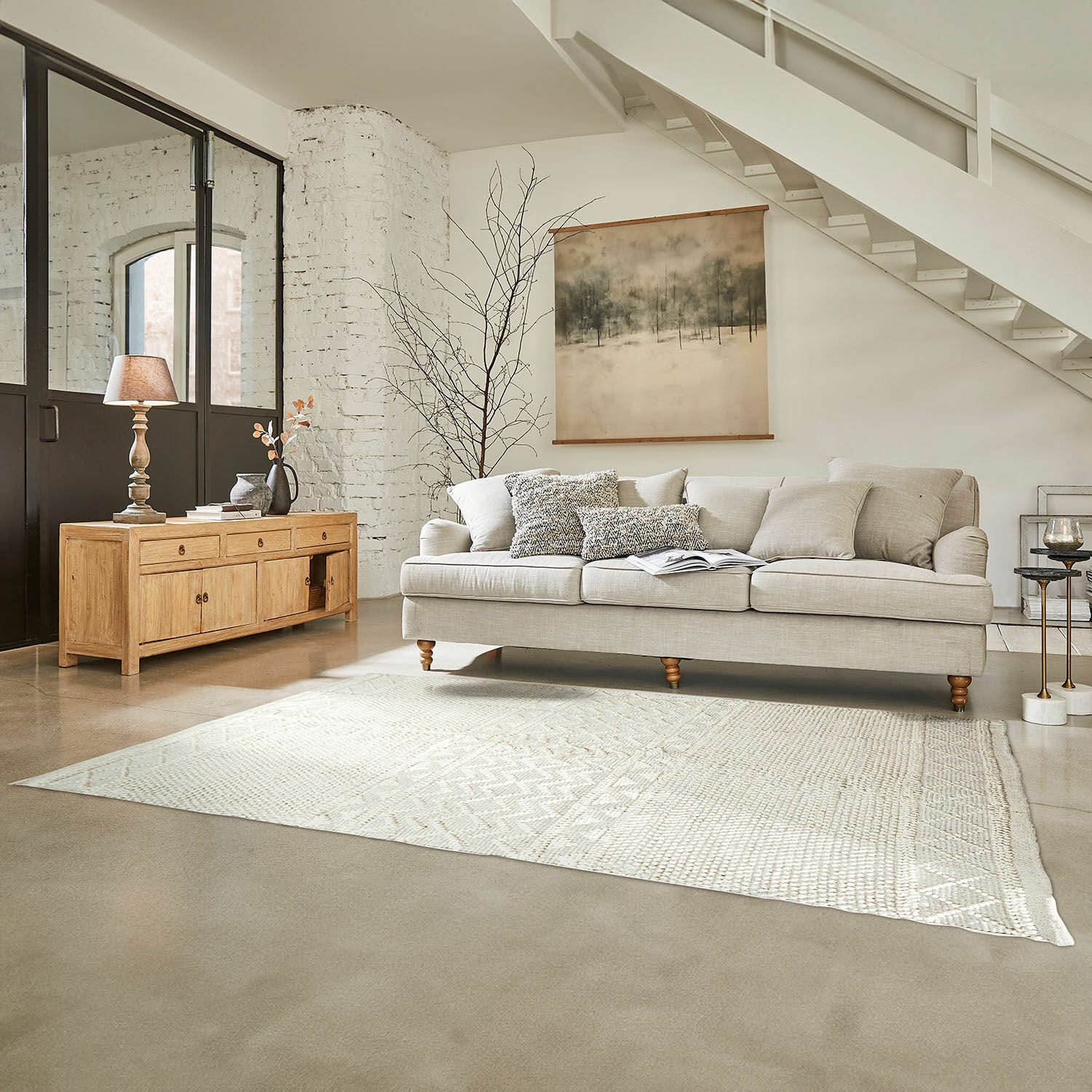 Tapis Hadir Canapé beige avec coussins et buffet en bois clair dans un salon lumineux avec tapis et décoration murale