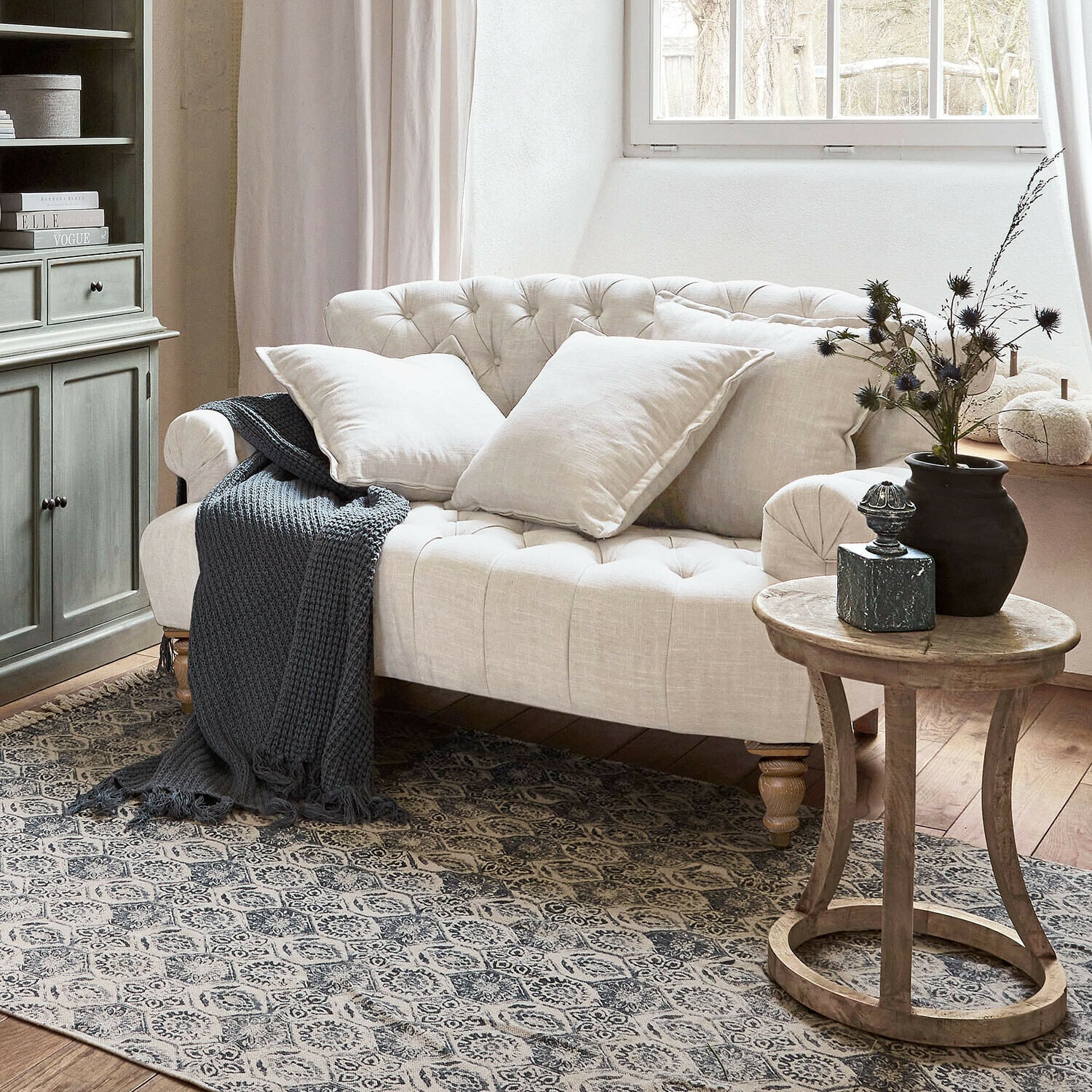 Canapé Springfield Village Canapé capitonné beige en lin avec coussins et plaid gris tricoté dans un salon chaleureux avec table en bois