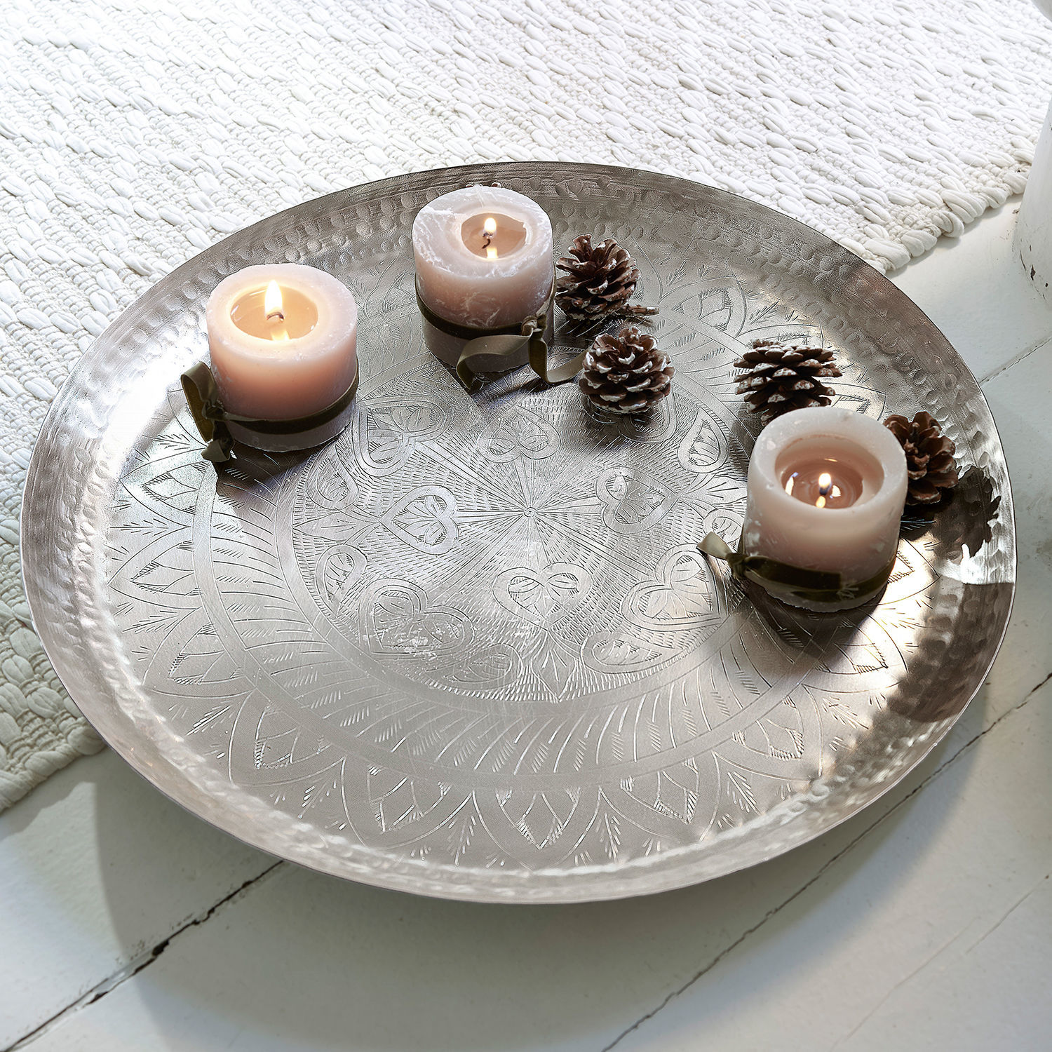 Plateau Moleur Plateau en métal gravé avec trois bougies roses et pommes de pin sur un sol blanc, décoration intérieure
