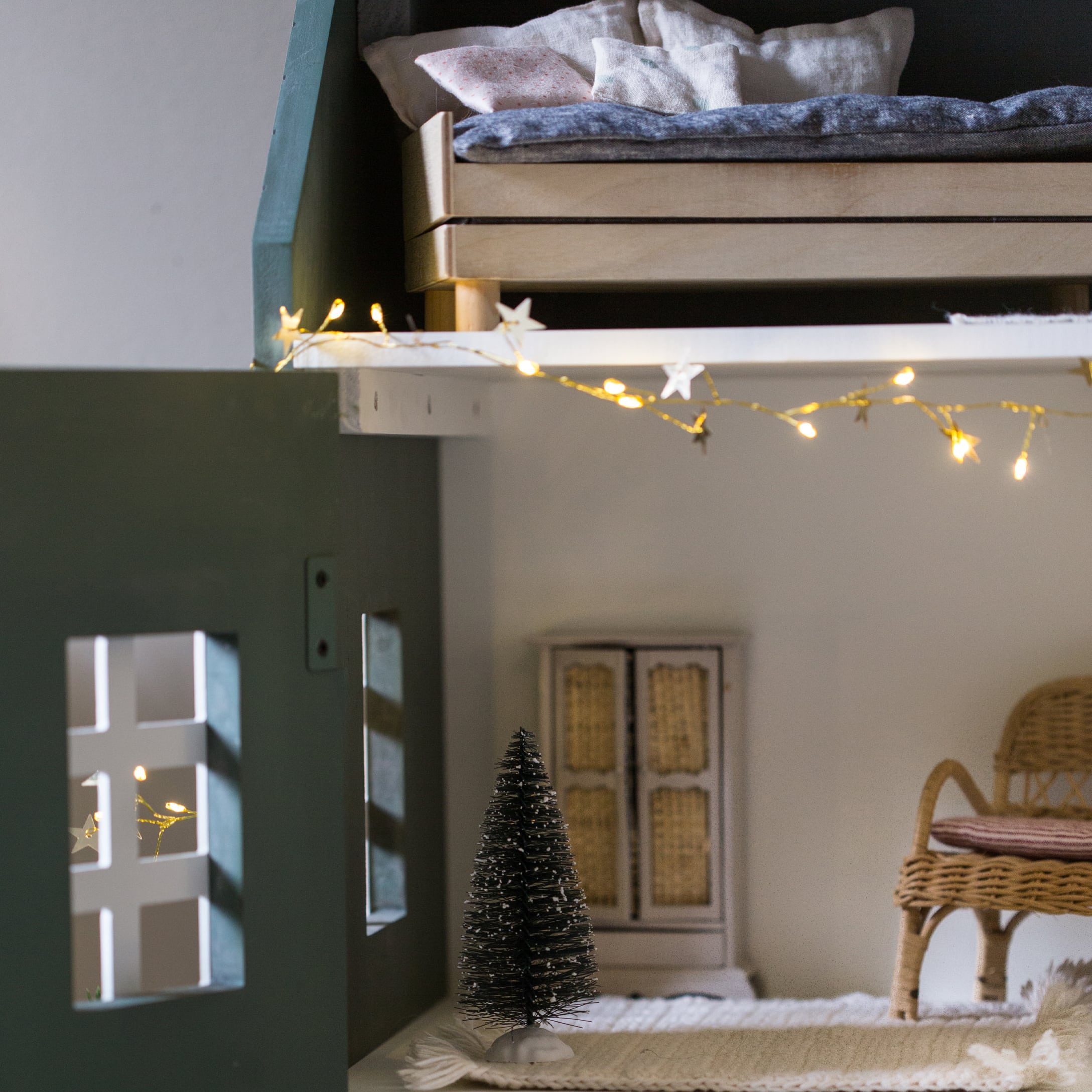 Petit sapin décoratif noir en fibre sur tapis blanc dans une chambre d'enfant chaleureuse avec guirlande lumineuse