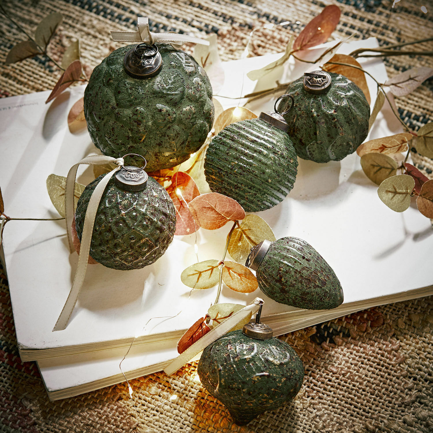 Lot de 6 décorations de Noël Moriches Ensemble de décorations de Noël vertes texturées avec rubans sur un livre blanc sur un tapis naturel