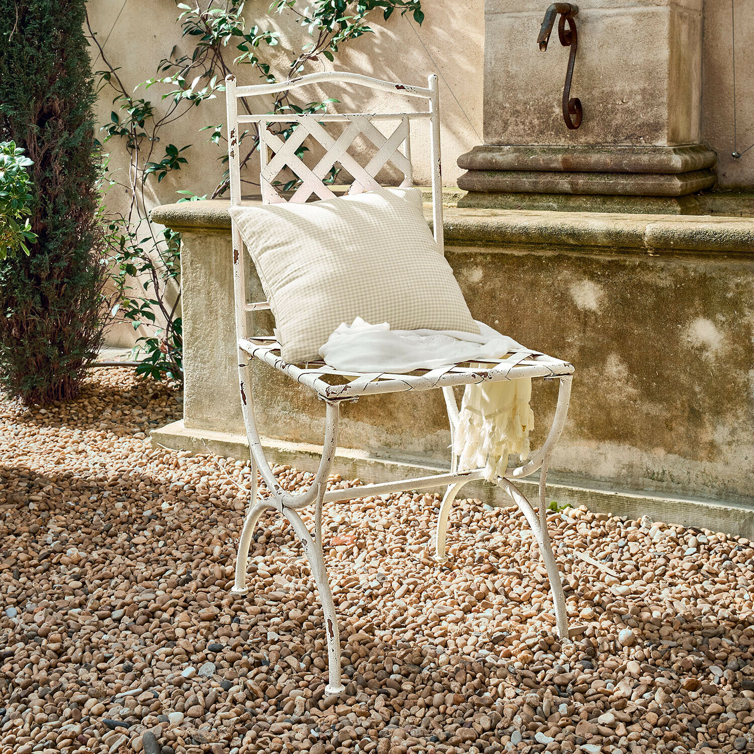 Chaise de jardin en métal blanc avec coussin à carreaux et étole légère sur sol en gravier