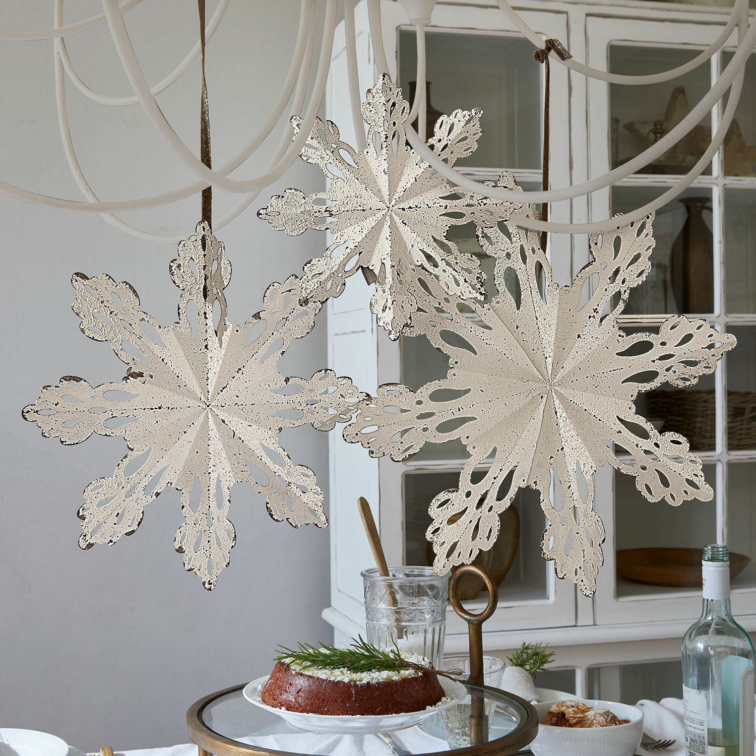 Lot de 3 décorations murales Lirvaya Flocons de neige décoratifs en métal crème suspendus dans une pièce claire avec gâteau sur la table