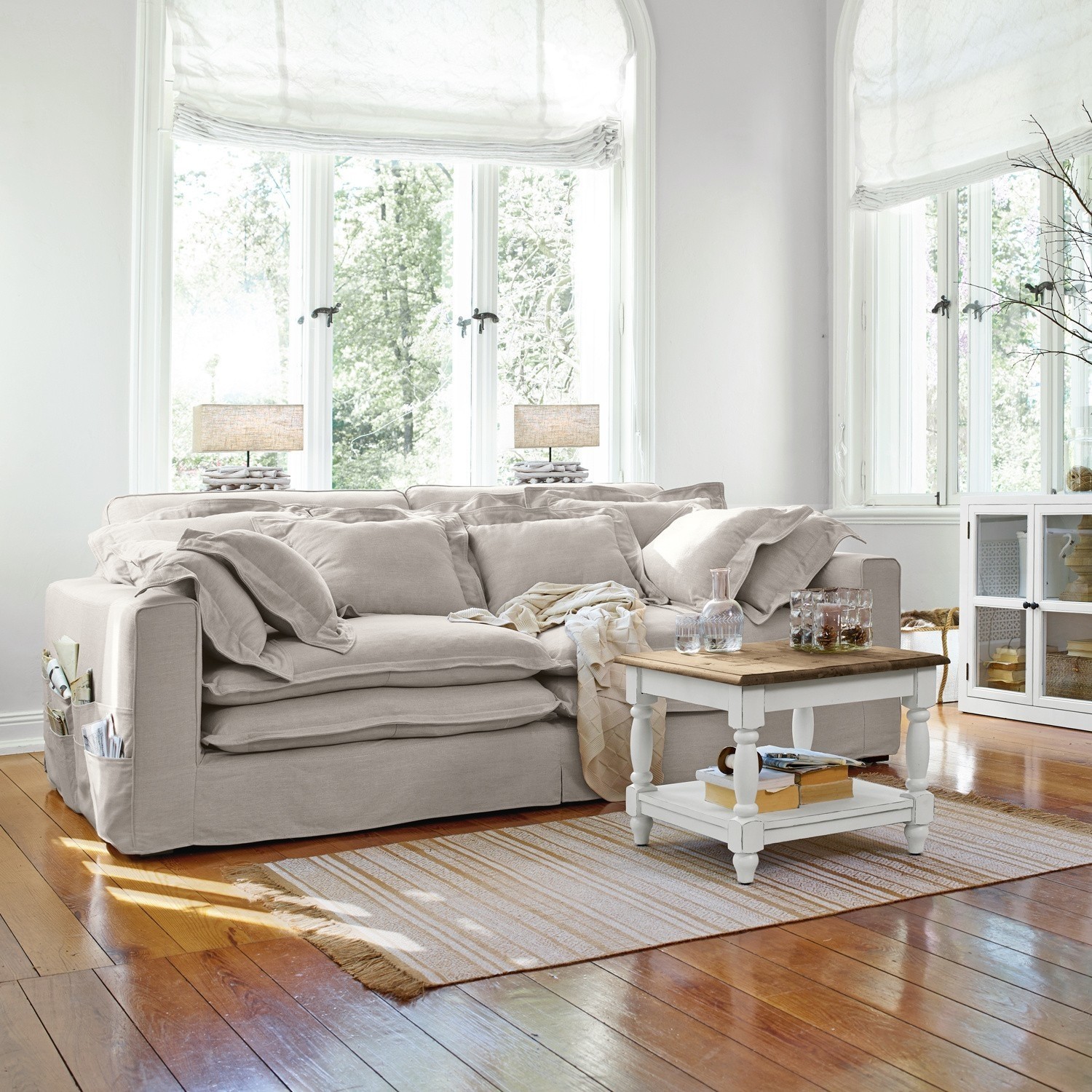Canapé beige en tissu avec coussins et table basse blanche sur parquet en bois dans un salon lumineux