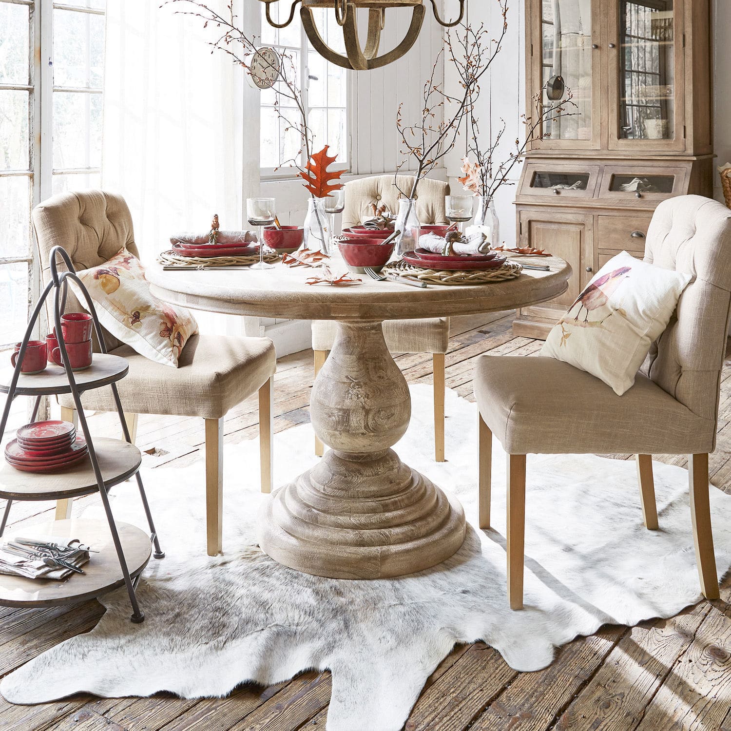 Tafel Orlin Lichte houten ronde tafel met beige gestoffeerde stoelen en rood servies in een lichte eetkamer