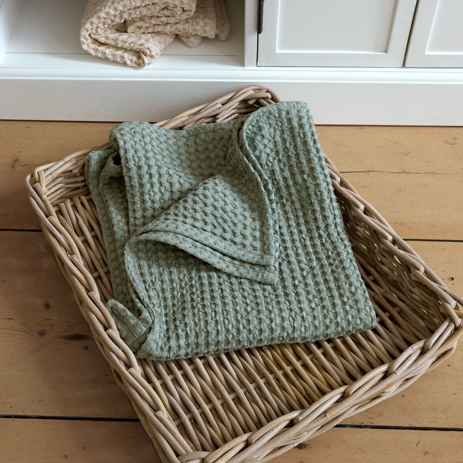 Serviette Maralei Plaid vert en coton gaufré dans un panier en osier posé sur un sol en bois clair
