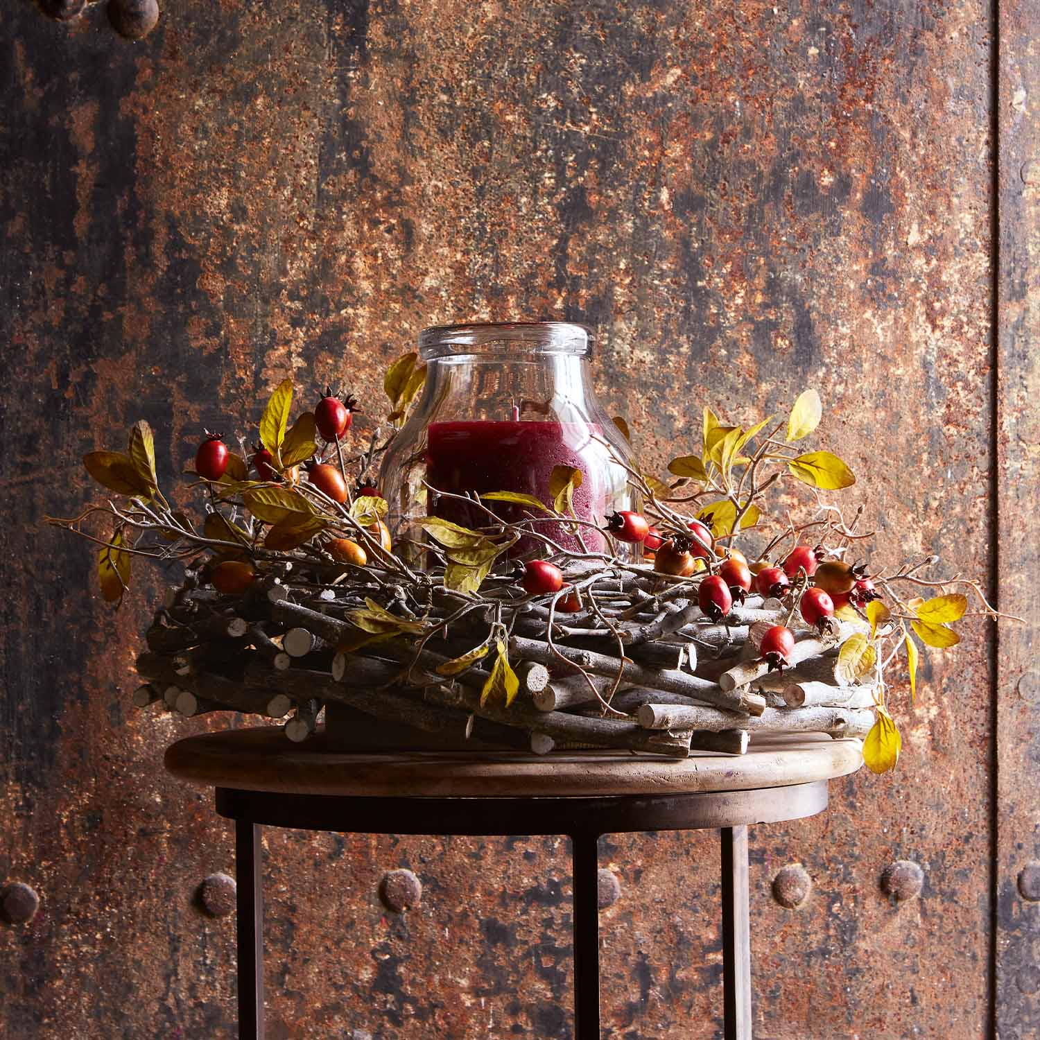 Decoratieve krans van takken met rode bessen en rode glazen kaars op houten tafel