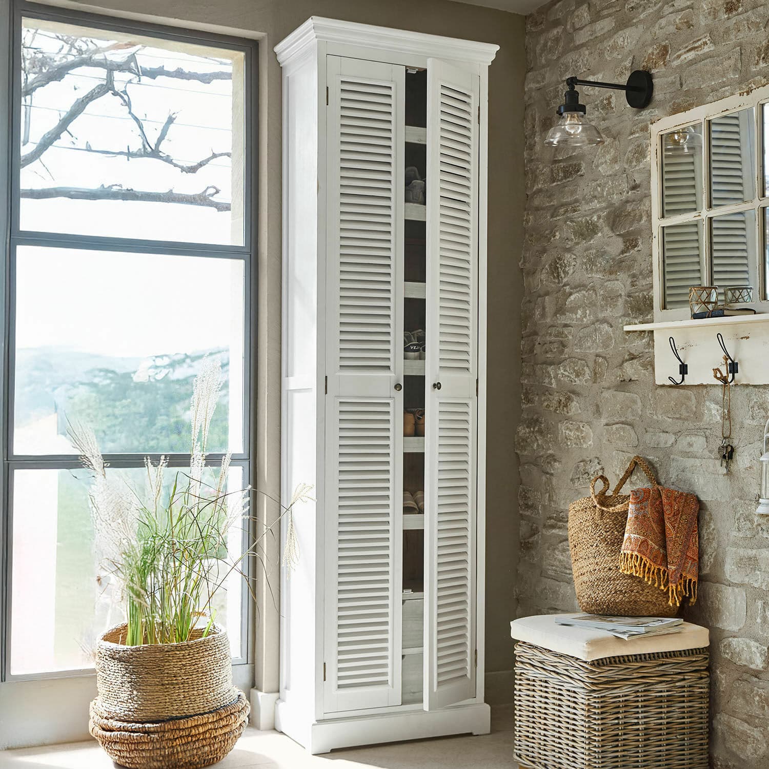 Meuble à chaussures Blossomby Armoire blanche en bois avec portes à persiennes dans un intérieur rustique avec mur en pierre