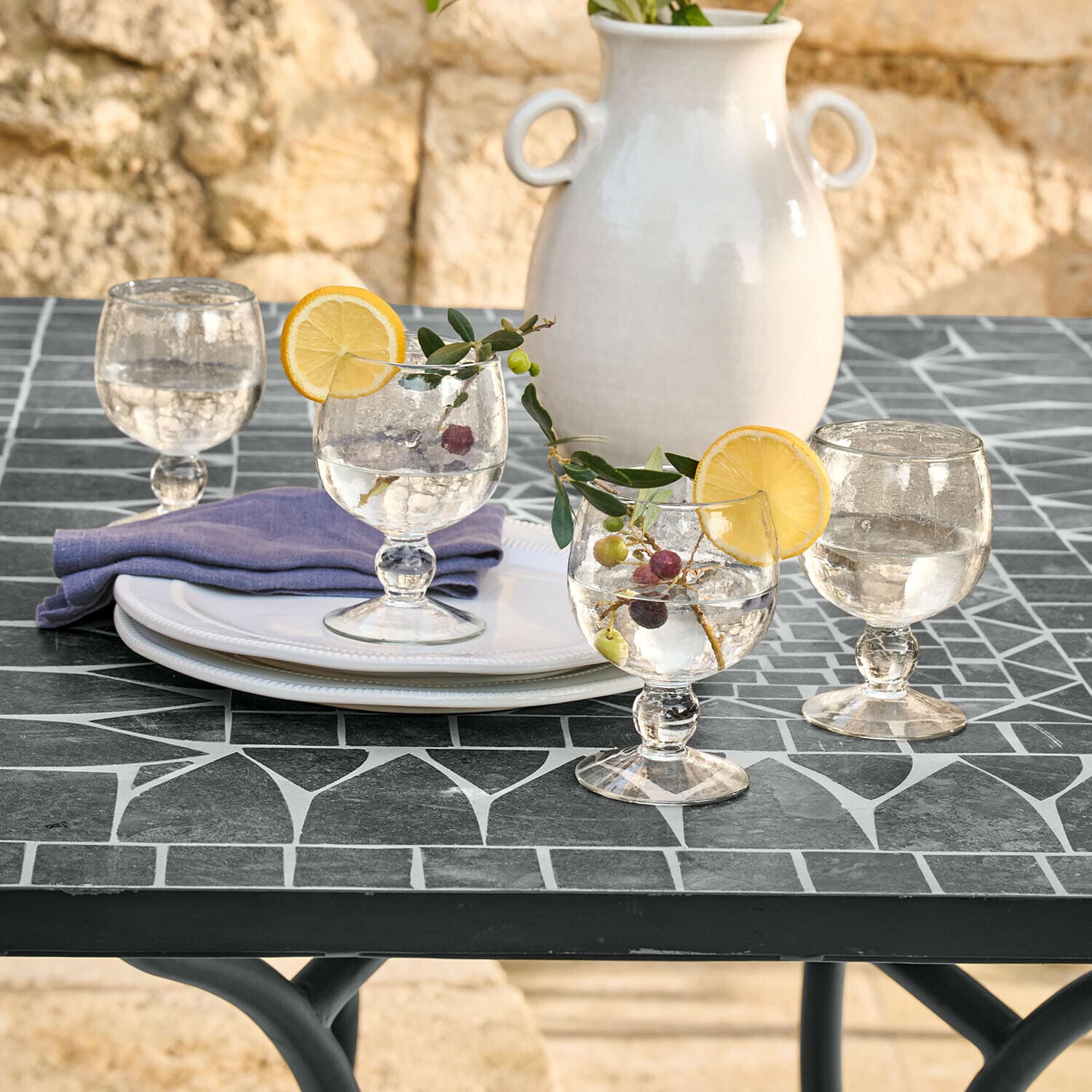 Lot de 4 verres Vinoros Verres en verre avec eau et tranches de citron sur table noire en mosaïque, vase en céramique blanche en arrière-plan