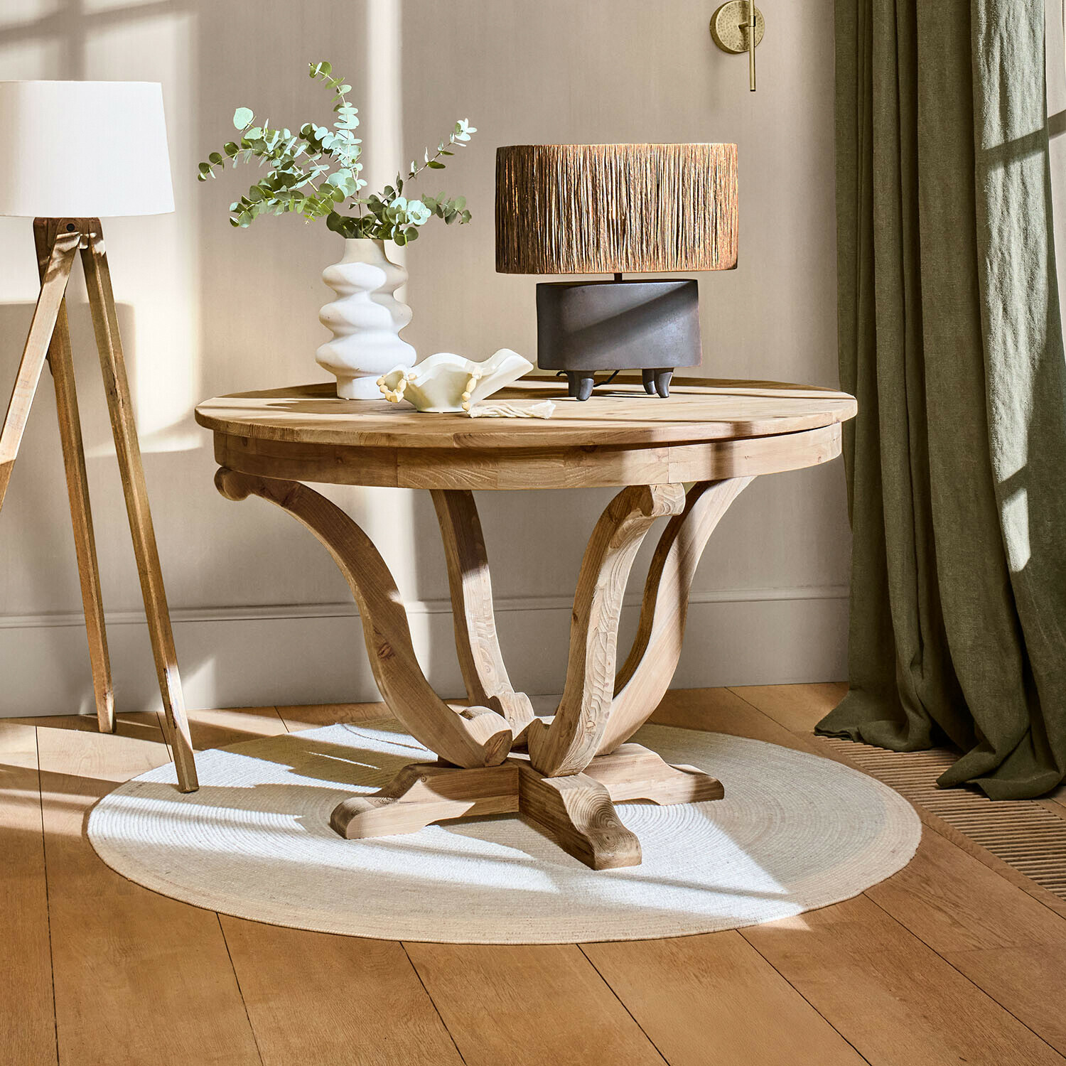 Table basse ronde en bois naturel sur tapis clair avec lampe et vase dans un salon lumineux