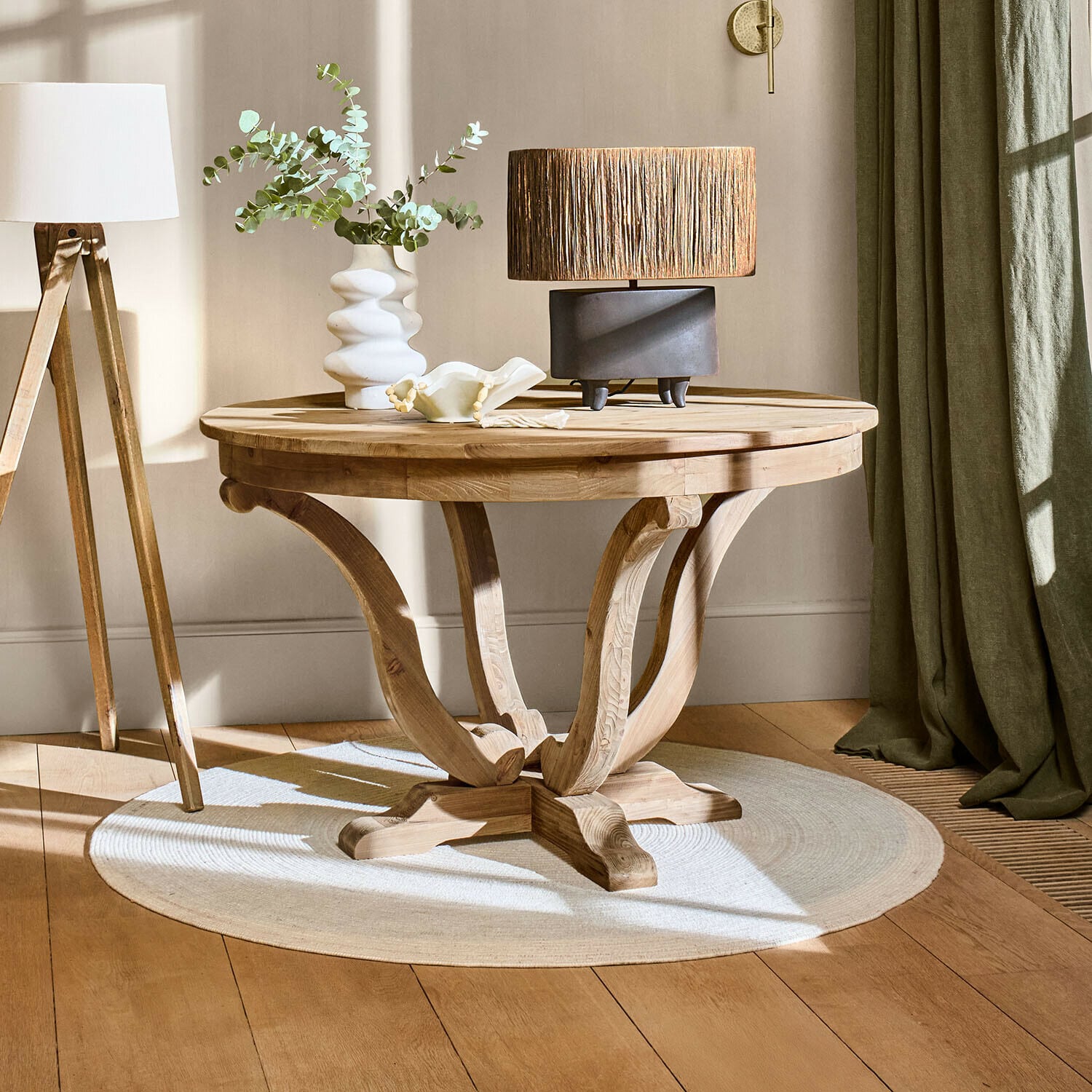 Table Oakminster Table basse ronde en bois naturel sur tapis clair avec lampe et vase dans un salon lumineux