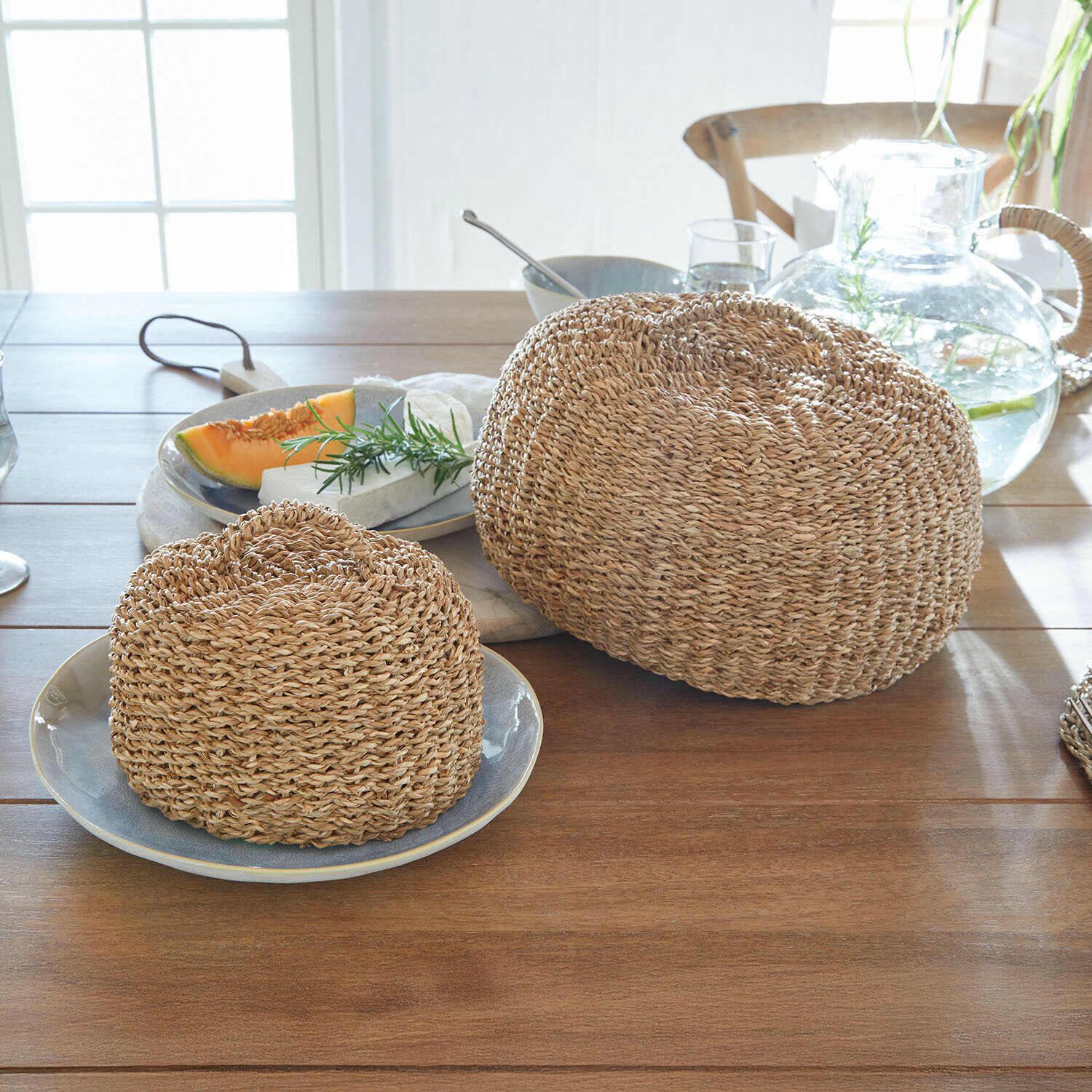 Vliegenkap set van 2 Sauvrelle Twee ronde broodkappen van gevlochten natuurlijk materiaal in beige op een lichte houten tafel