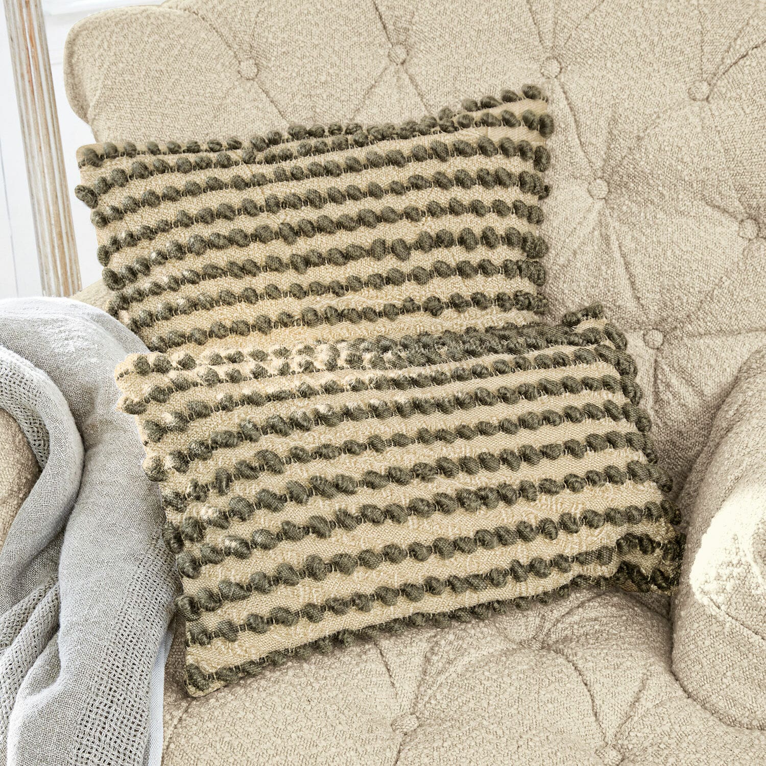 Beige sierkussen met groene pompons op beige gestoffeerde stoel, woontextiel