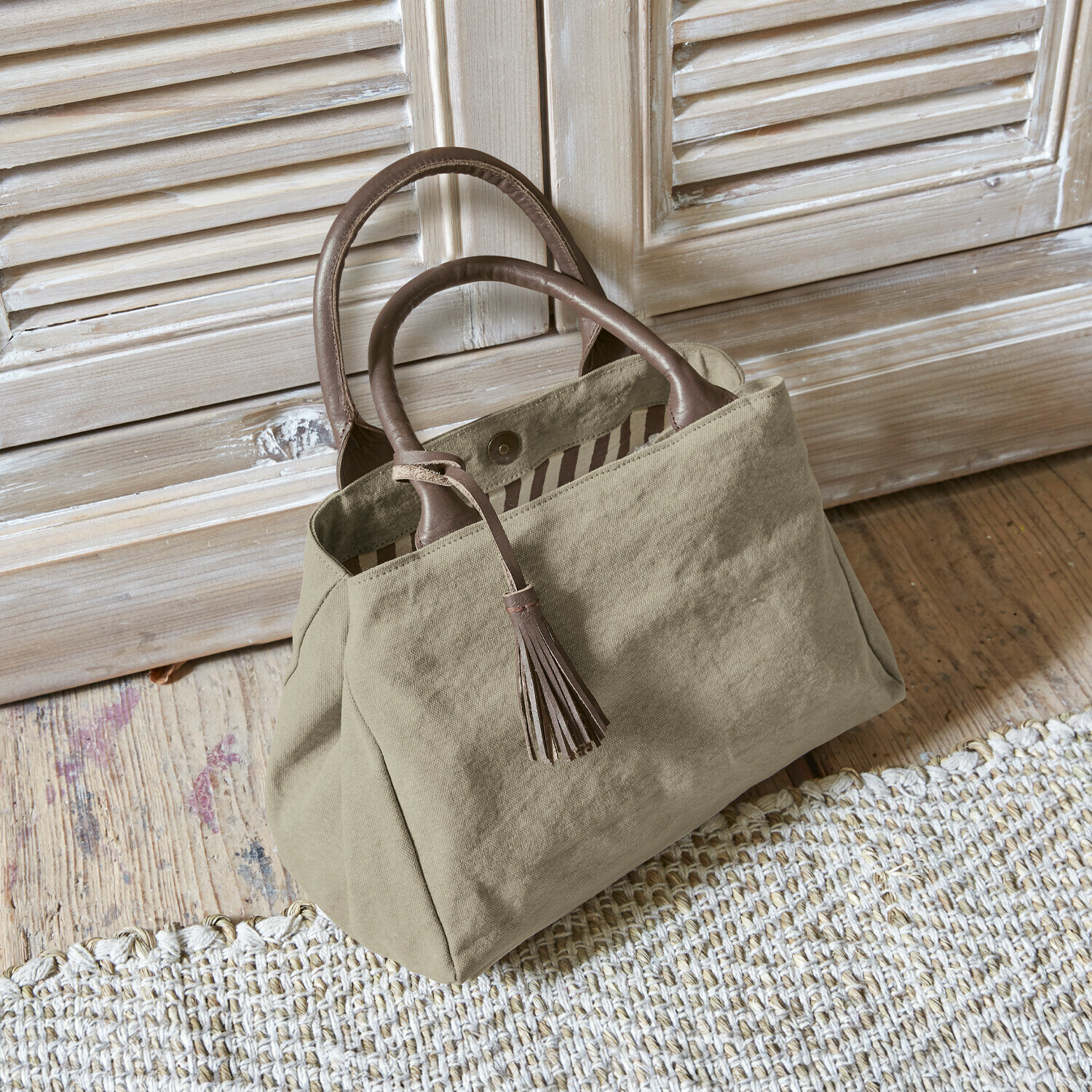 Tas Hoya Beige stoffen tas met bruine leren handvatten en kwast op houten vloer