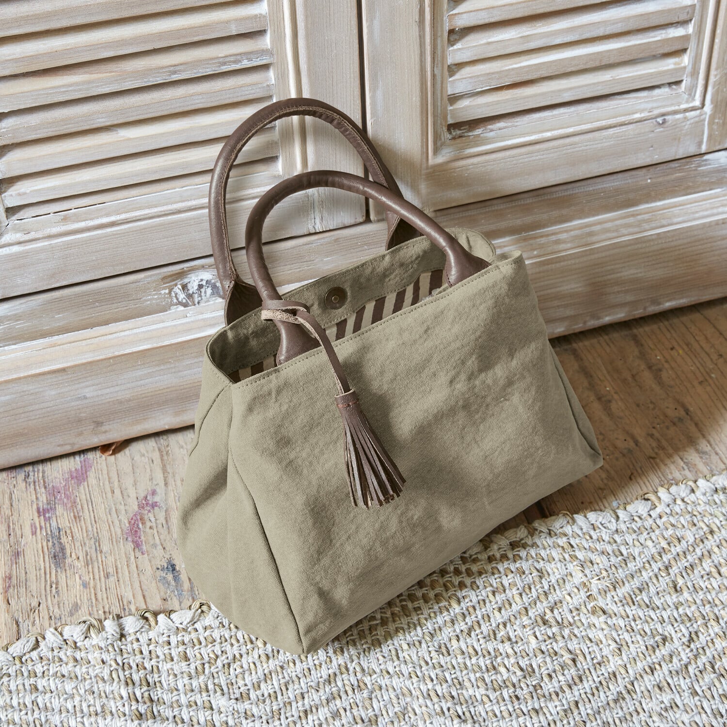 Tas Hoya Beige stoffen tas met bruine leren handvatten en kwast op houten vloer
